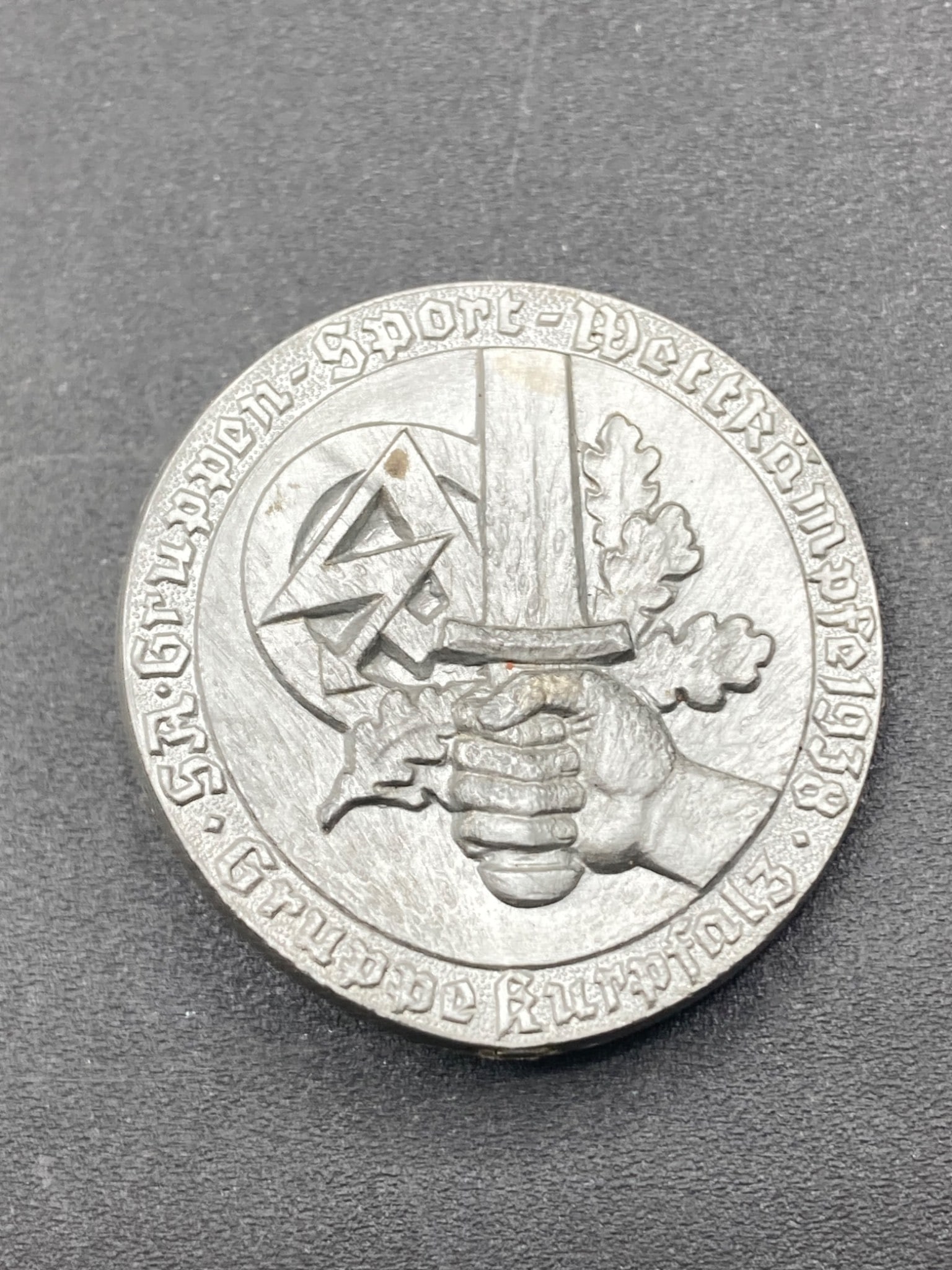 1938 German SA Sports Tinnie by Richard Sieper & Sohne: This is a German SA Sports Tinnie from 1938. The front depicts an oak leaf design, a hand gripping a sword, and the SA logo, with lettering reading 'Gau Baden-Pfalz' and 'SA Grupen Sport Wettkampf 193