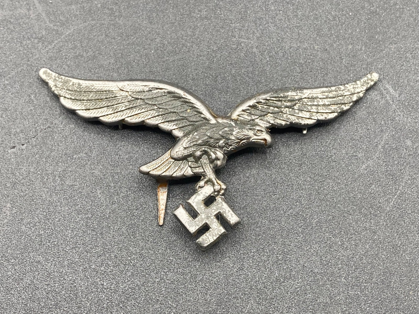 WWII German Army Officer Cap Badge: A WWII German Army Officer Cap Badge featuring a metal eagle holding a Swastika. The badge ais cast in metal, with attachment prongs visible on the back. This item reflects the standard design used fo