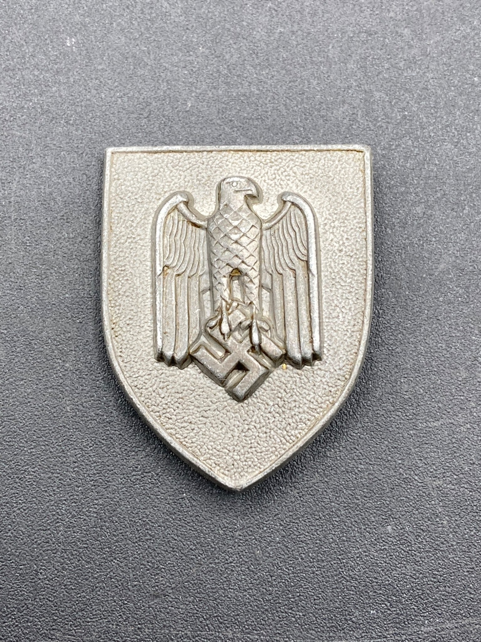 WWII German Army Marksmanship Lanyard Badge: This item is a WWII German Army Marksmanship Lanyard Badge. It features the iconic eagle emblem holding a swastika, cast in a metal alloy material. The reverse side includes two attachment hooks, show