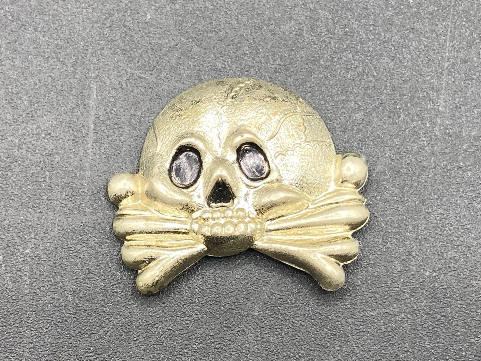 WWII German Army Officer Totenkopf Insignia Pin: WWII German Army Officer Totenkopf insignia pin. Features the Danzig skull and crossbones motif associated with the Totenkopf division. Pin measures 1 1/4 inches wide. Constructed of metal, with visib