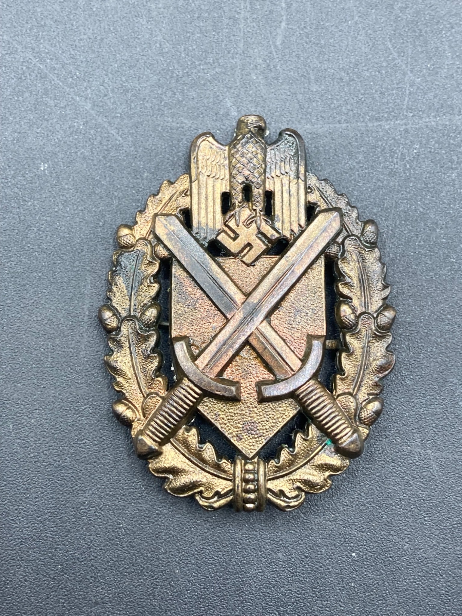 WWII German Wehrmacht Army Officer Marksman Lanyard Badge: This item is a WWII-era German Wehrmacht Army Officer Marksman Lanyard Badge. It features a detailed crossed sword design over a shield with oak leaf motifs and overhead eagle insignia. The piece appe