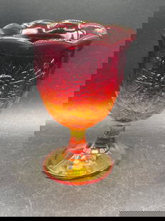 Amberina Glass Goblet with Raised Grape and Leaf Design: This is an Amberina glass goblet with a vibrant gradient of deep red to yellow. The goblet features a detailed raised grape and leaf design on its bowl, with a scalloped rim and pedestal base. It