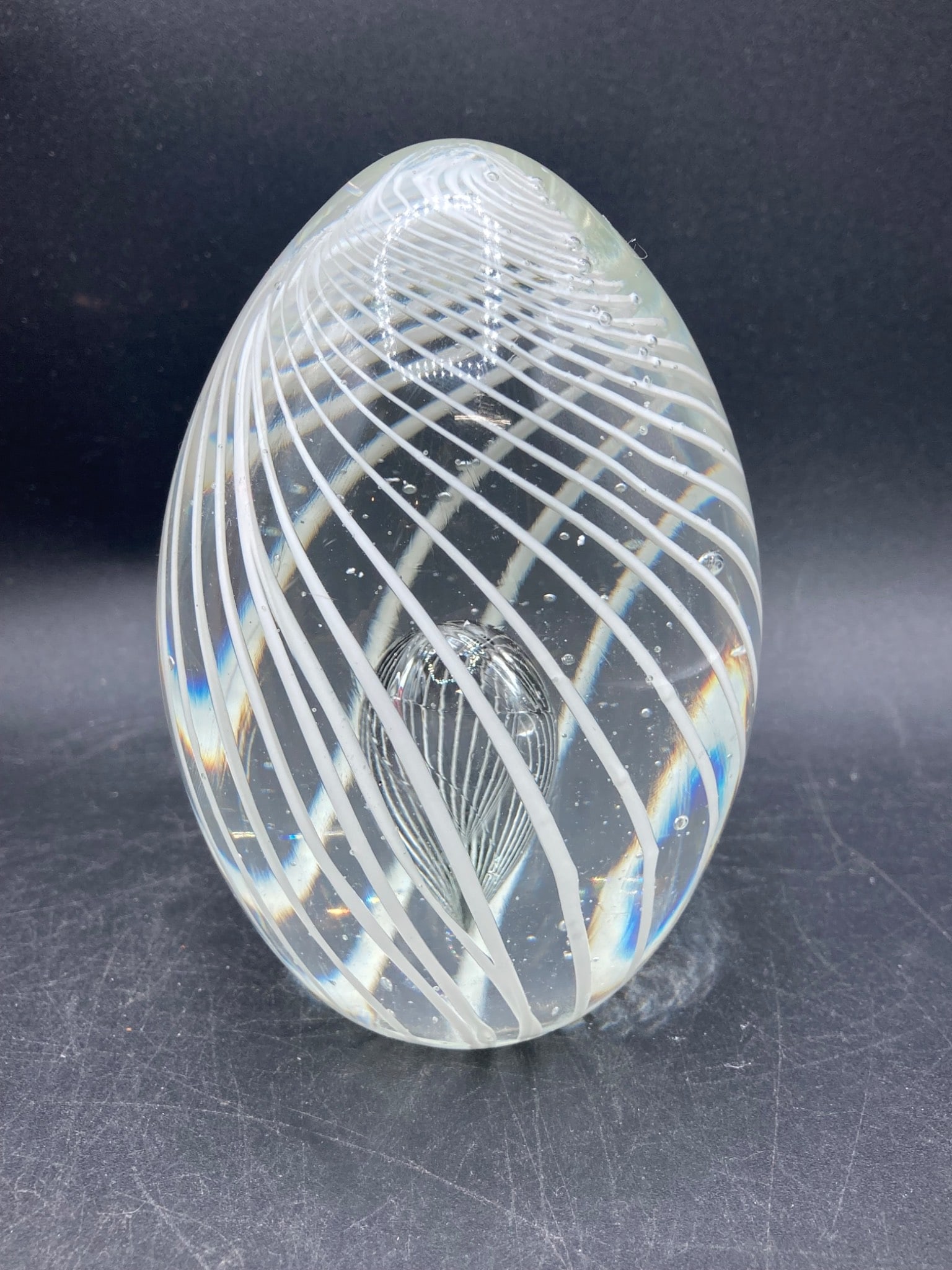 Murano Glass Paperweight with Swirled White Design: This Murano glass paperweight features a clear exterior with a refined white swirled pattern and an intricate teardrop-like internal design. The base includes a label reading 'Italy Design,' indicatin
