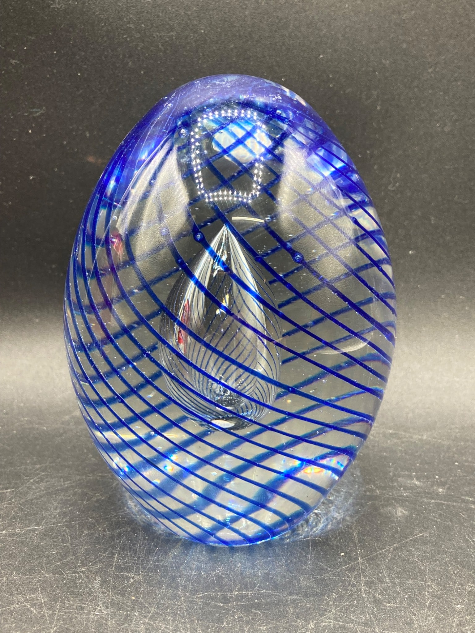 Murano Glass Paperweight with Blue Spiral Design: Murano glass paperweight featuring an elongated oval form with internal blue spiral patterns encircling clear glass and a suspended teardrop-shaped element. Approximate dimensions: 4 inches in height.