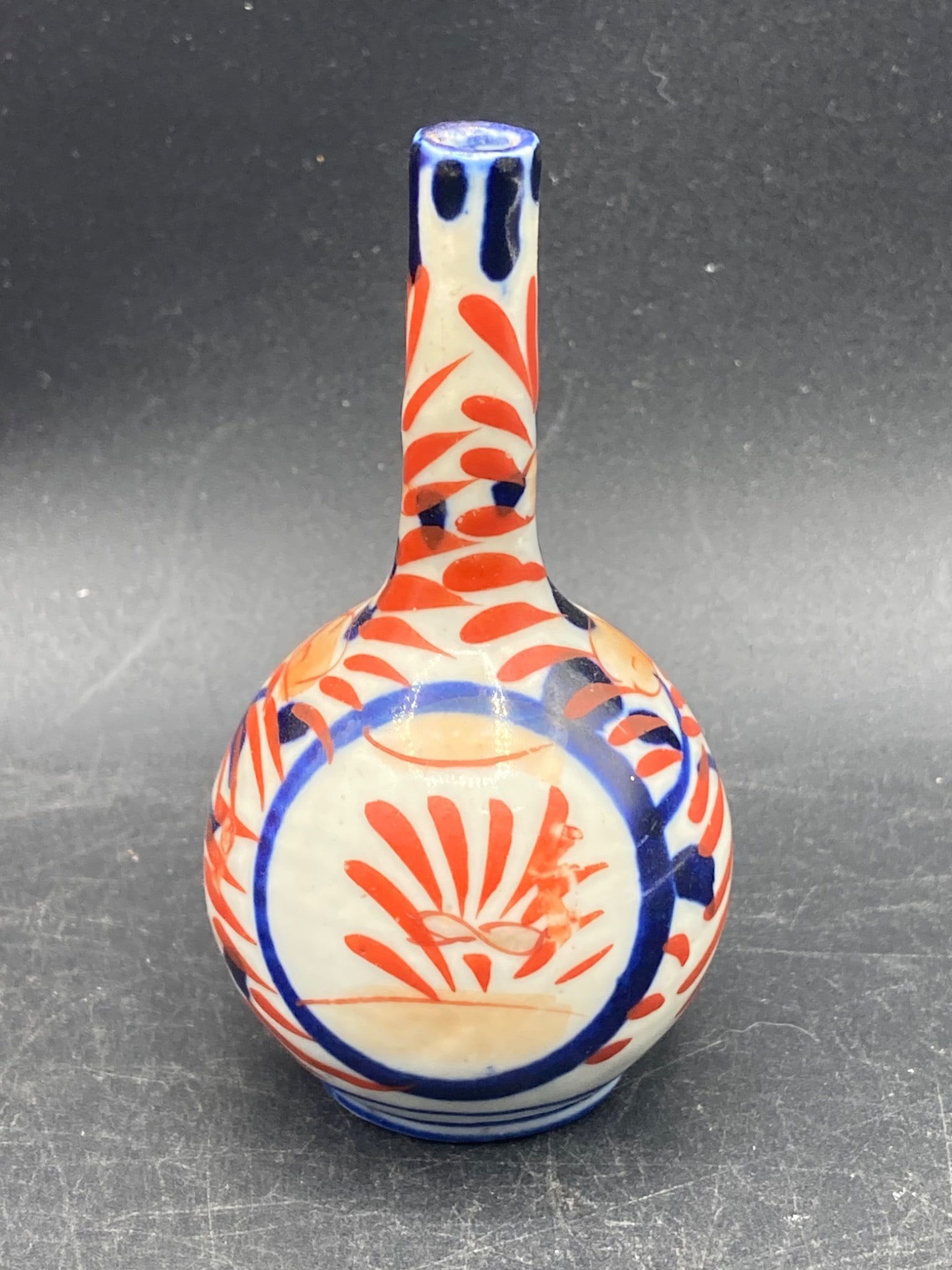 Japanese Imari Porcelain Miniature Vase with Floral Motifs: This is a Japanese Imari porcelain miniature vase featuring a traditional floral and red-blue pattern design. The vase has a narrow neck and rounded body with intricate detailing characteristic of the