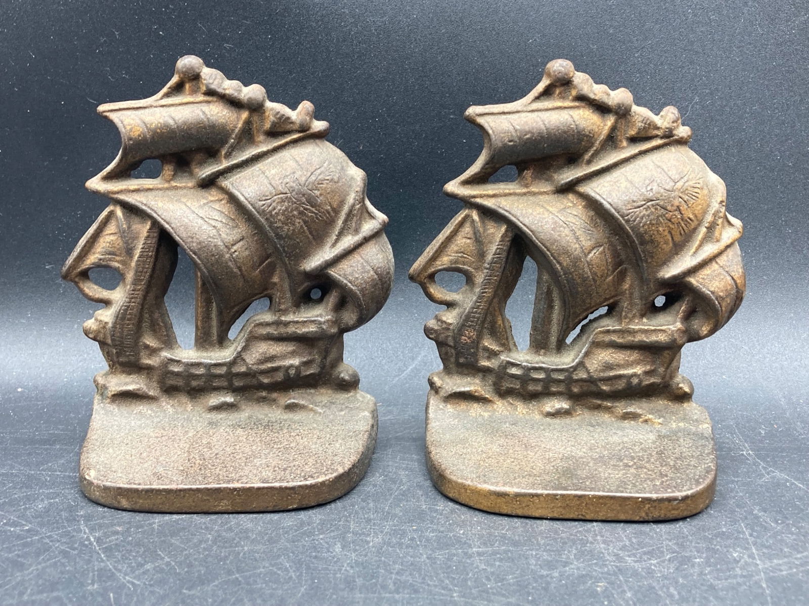 Antique Brass Spanish Armada Ship Bookends: Antique brass bookends featuring a depiction of a Spanish Armada ship. Each piece is intricately designed to resemble a sailing ship with detailed sails and structure. The set is made of brass with a