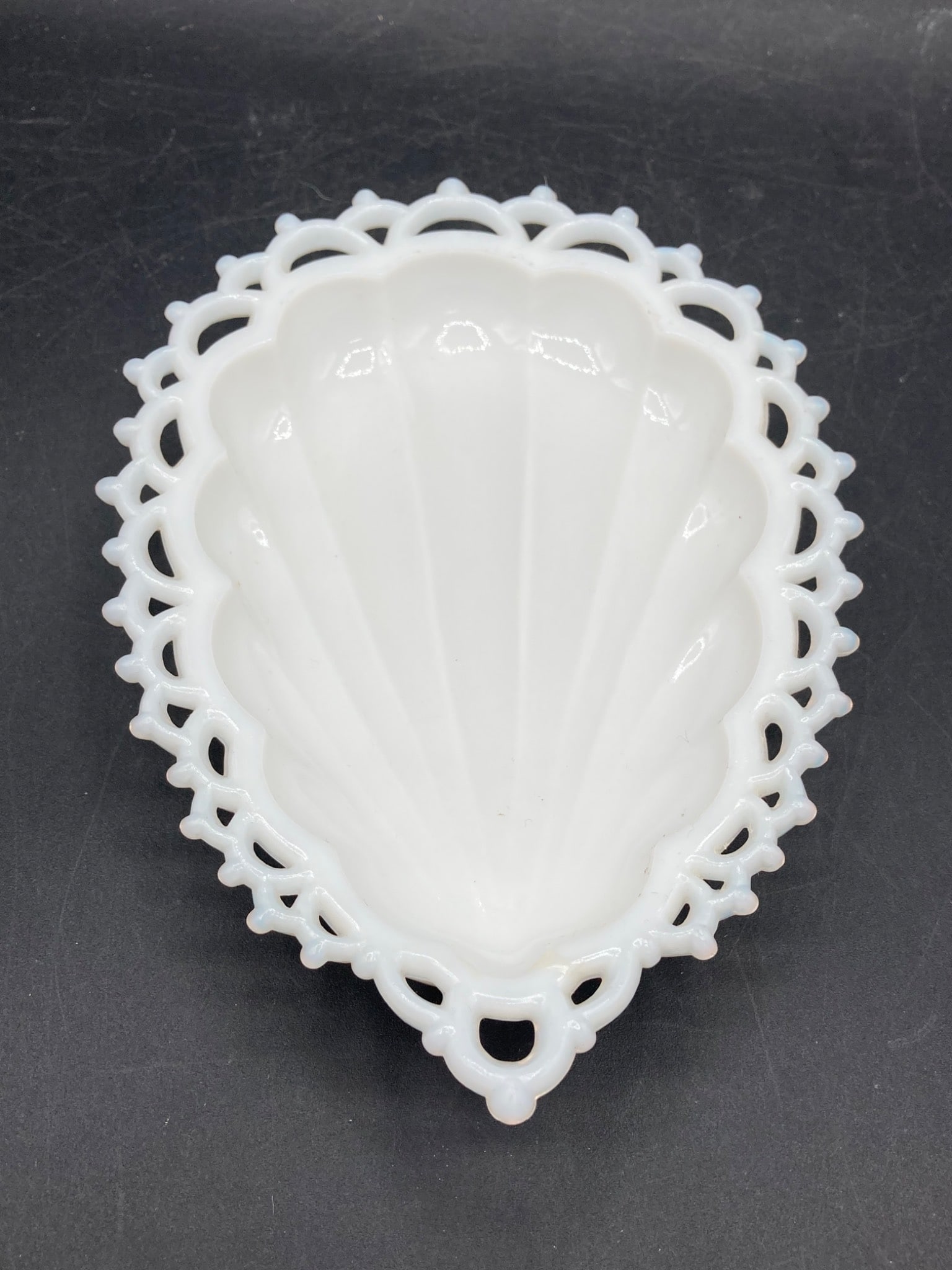 Westmoreland Milk Glass Seashell Dish with Reticulated Edge: This is a Westmoreland Milk Glass Seashell Dish featuring a reticulated edge design. The milk glass is finished in a glossy white and showcases a seashell shape. The underside bears the Westmoreland G