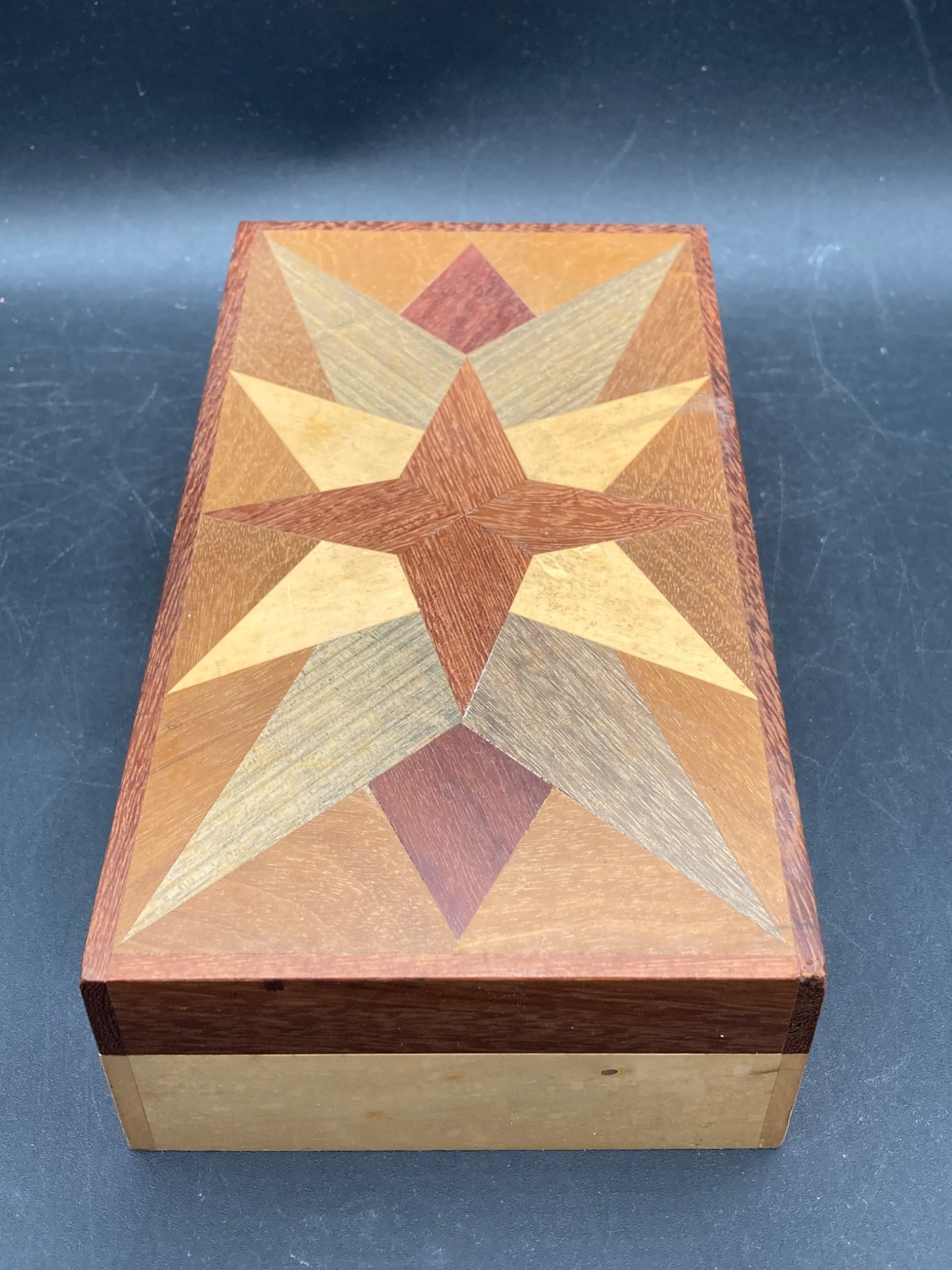 Handcrafted Wooden Marquetry Star Box: A rectangular wooden box featuring a marquetry star design on the lid. The box is constructed from multiple wood types, showcasing contrasting tones, and features a removable lid. Measurements are app
