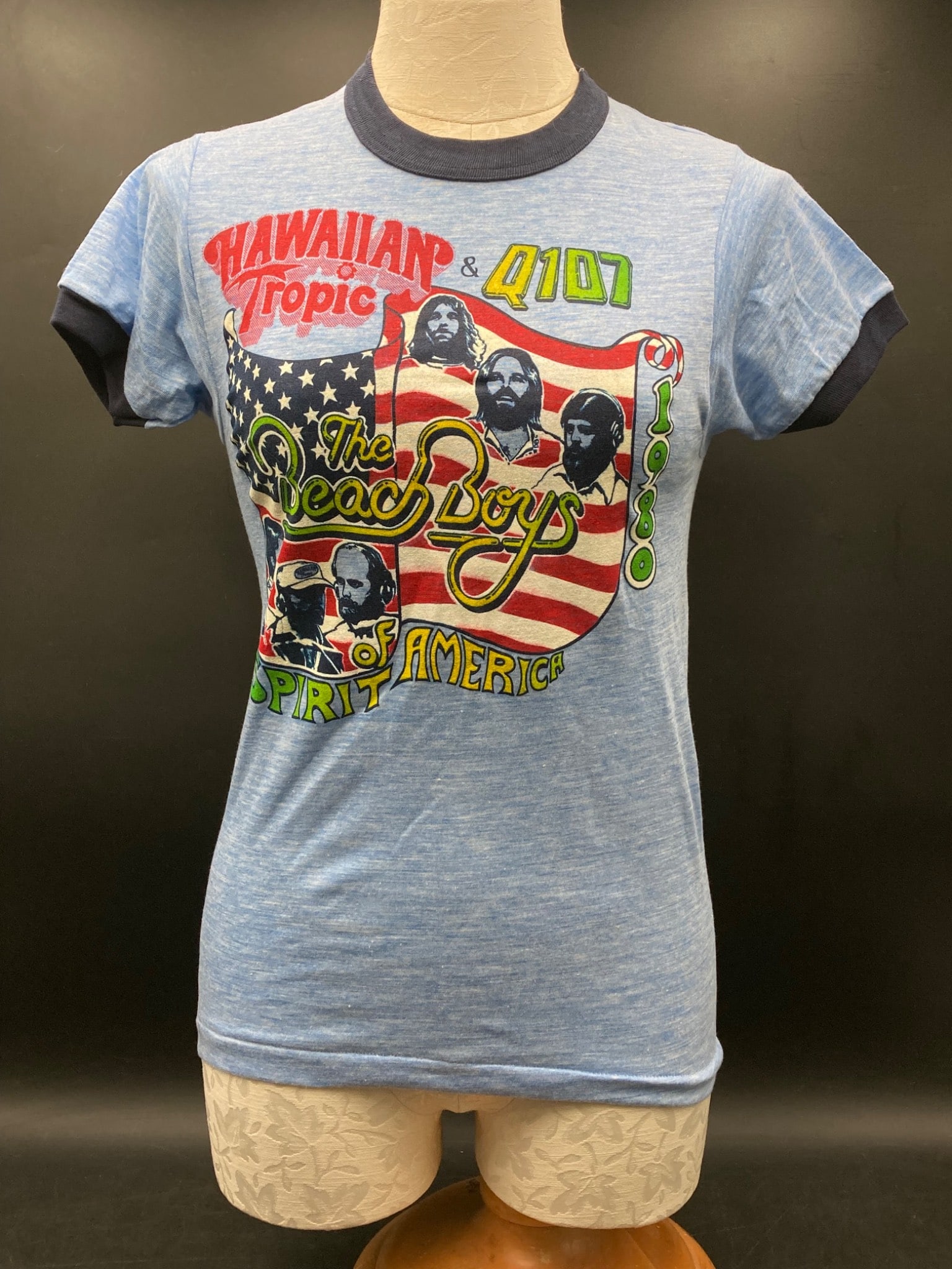 1980 Hawaiian Tropic Beach Boys Spirit of America T-Shirt, Small: This is a 1980 Hawaiian Tropic & Q107 promotional T-shirt featuring graphics of The Beach Boys with ‘Spirit of America’ text. Made from 50% cotton and 50% polyester, the size is small (34-36), as