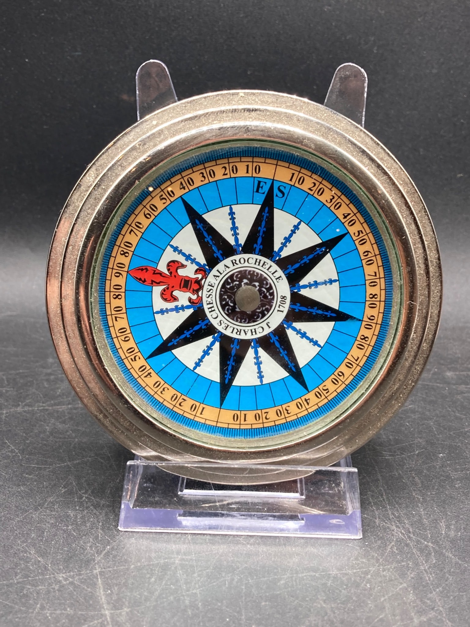 Charles La Rochelle 1708 Design Desk Compass: This is a circular metal compass with a decorative face featuring a fleur-de-lis motif and 'Charles La Rochelle 1708' inscription. The face includes a numerical ring with readings and directional text