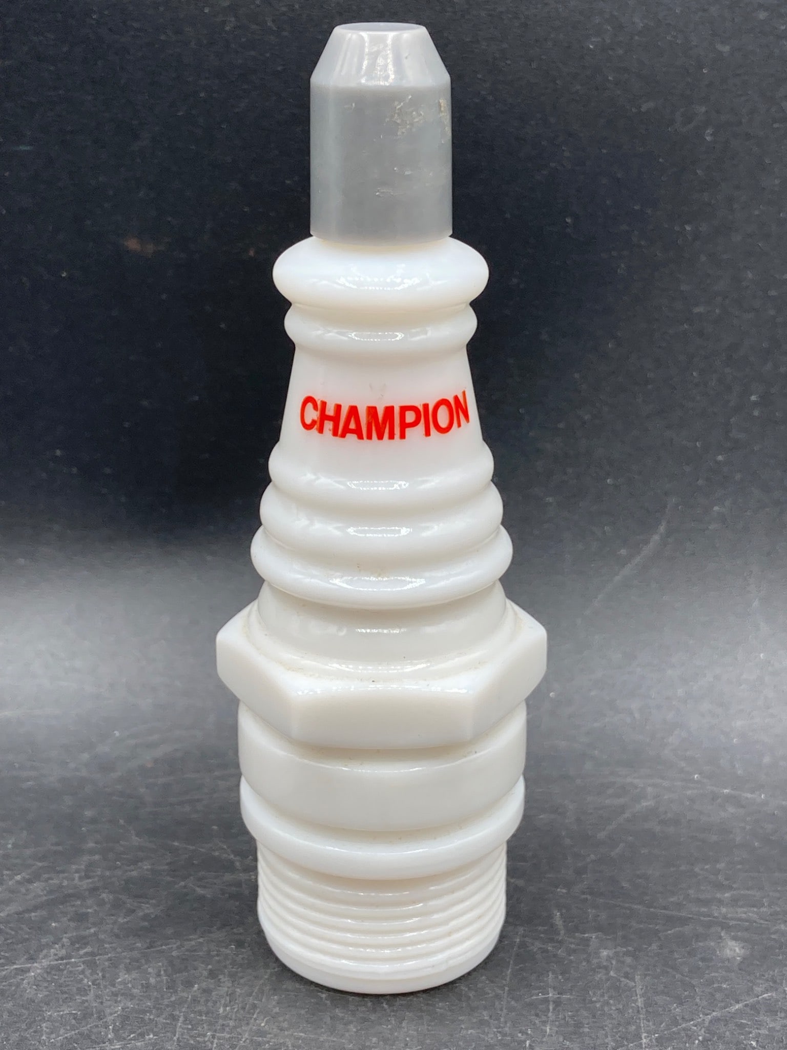 Avon Champion Spark Plug Shaped Cologne Bottle: This item is an Avon glass cologne bottle shaped like a spark plug, featuring the text 'CHAMPION' in red. The base of the bottle is marked with 'AVON,' providing manufacturer identification. The bottl