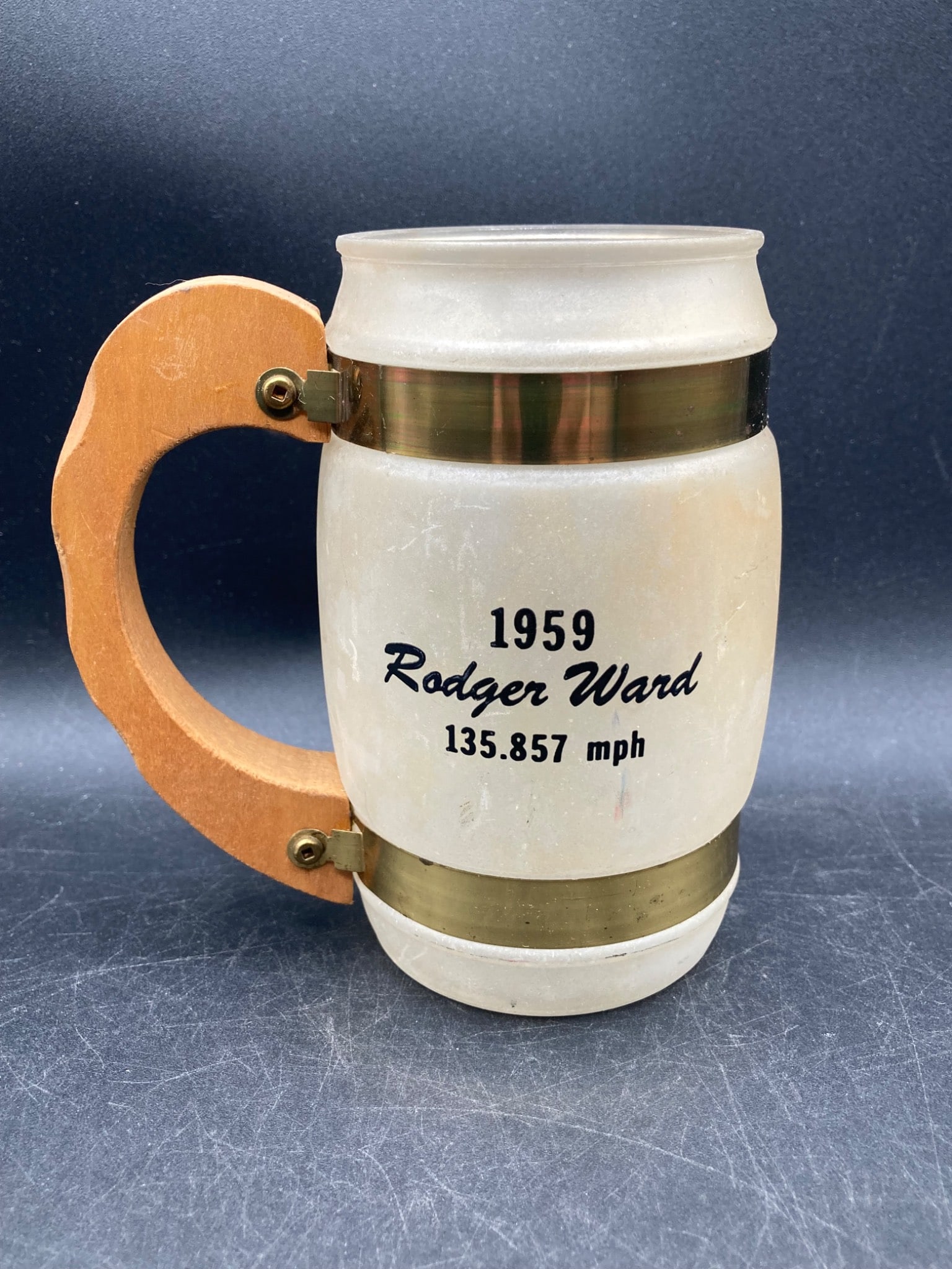 Siesta Ware 1959 Indy 500 Winner Rodger Ward Mug: This is a Siesta Ware commemorative mug celebrating Rodger Ward, the 1959 Indy 500 winner with an average speed of 135.857 mph. The mug features a frosted glass body with a wooden handle and brass acc