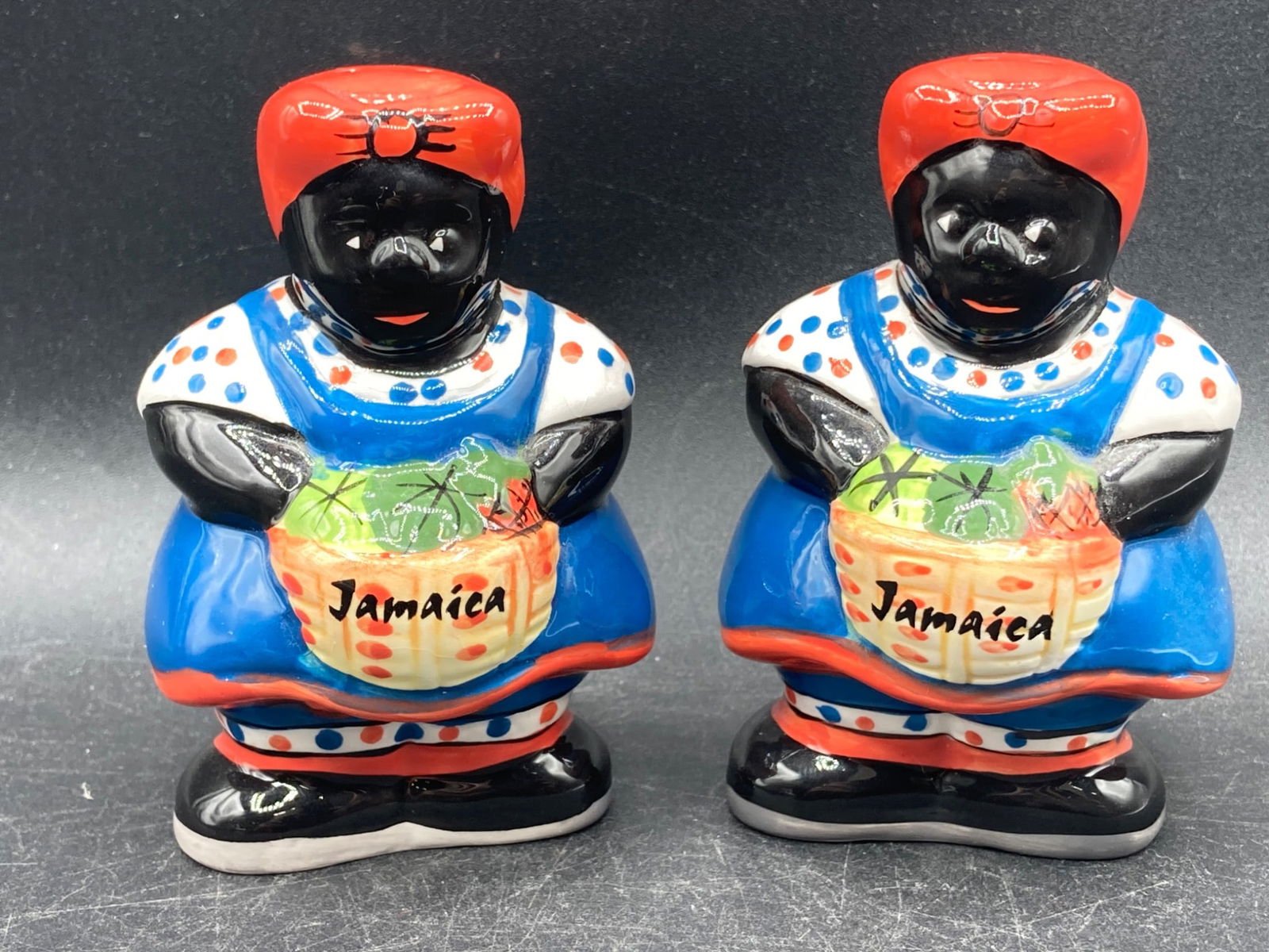 Black Americana Jamaica Porcelain Salt & Pepper Shaker Set: This is a Black Americana Jamaica-themed porcelain salt and pepper shaker set. Both shakers feature a vibrant design with 'Jamaica' printed on the front. The bottom markings read '@agiftcorp'. They me