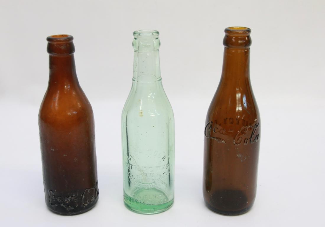 GROUP LOT OF COCA COLA BOTTLES: (2) AMBER AND GREEN BOTTLES - STRAIGHT SIDED COCA COLA BOTTLE IN AMBER CINCINNATI, OHIO - STRAIGHT SIDED IN CURSIVE CANTON, OHIO - GREEN COCA COLA COSHOCTON, OHIO Dimensions: 7" - 7 1/4" - 7 3/4"