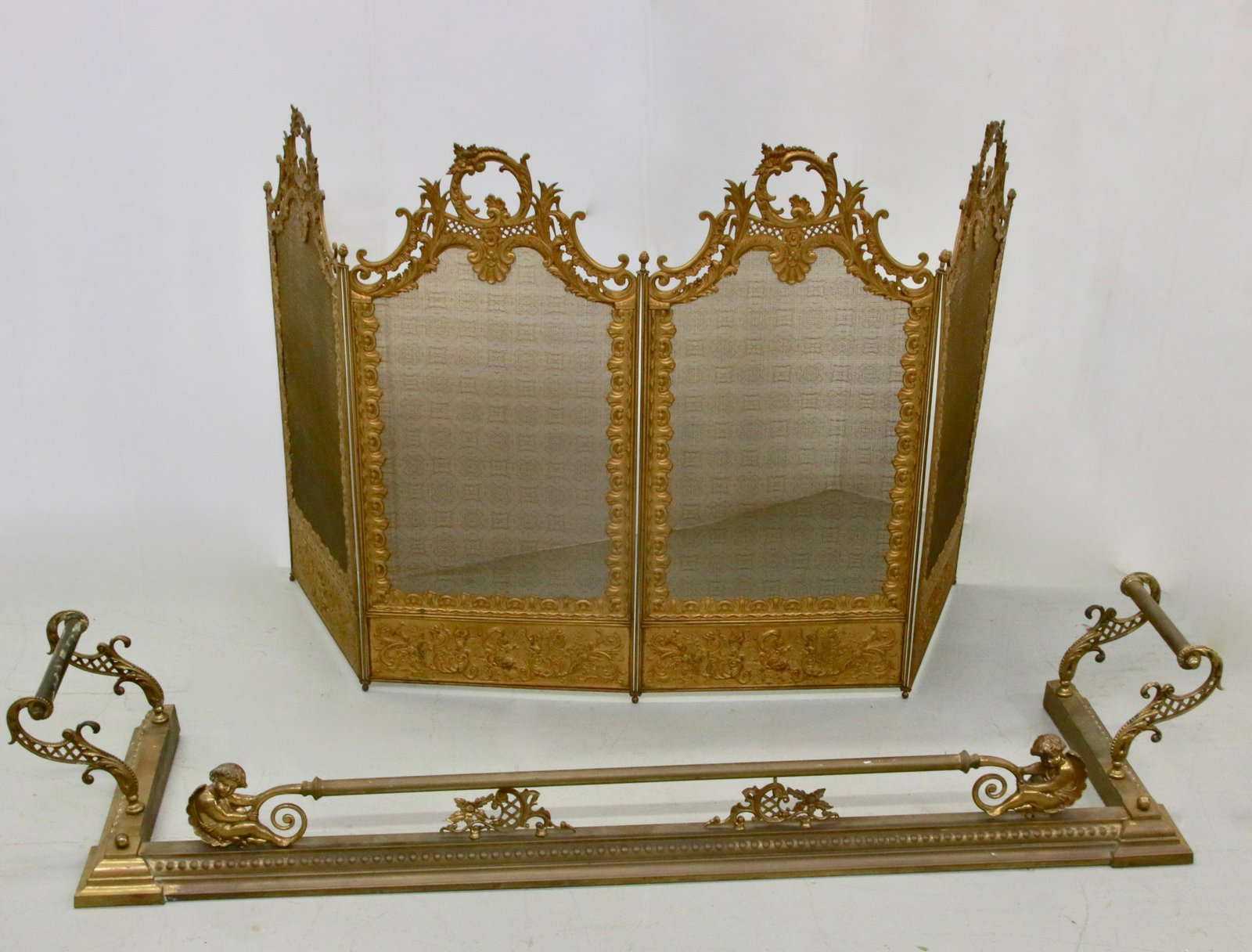 BRASS FIREPLACE SCREEN AND FENDER: FOLDING FIREPLACE SCREEN AND FENDER - CHERUB MOTIF ON FENDER Size: SCREEN 58" X 31" - FENDER 51 1/2" X 14 1/2" D X 8 1/2" H