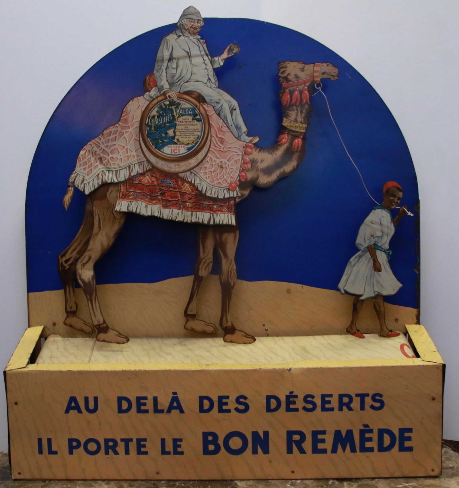 VINTAGE 1930S ADVERTISING AUTOMATON FOR A PHARMACY: LITHOGRAPHED TIN. MADE IN FRANCE. BOTTOM BANNER MOVES, CAMEL LEGS AND BOY LEADING CAMEL. ELECTRIC CHORD IN WORKING ORDER. Size: 32" X 8" X 36"