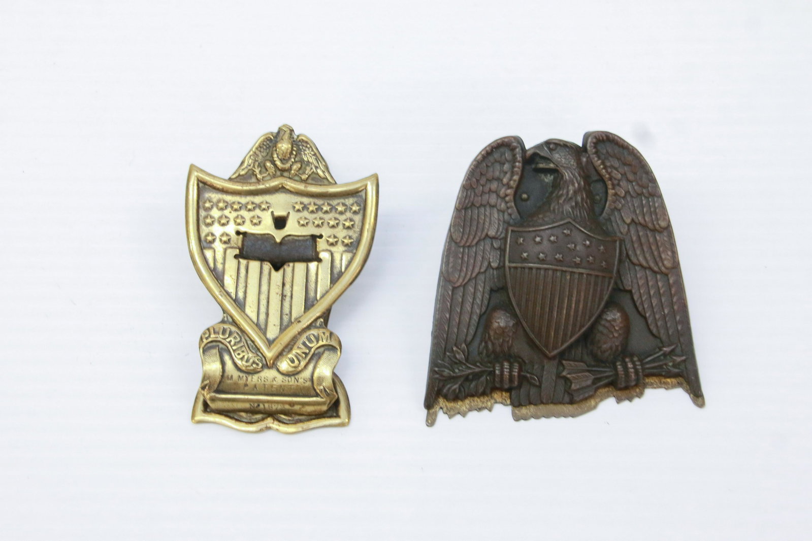 PAIR OF METAL BRASS CLIPS: INCLUDING: EAGLE WITH SHIELD AND SHIELD MRKD. "PATENT" ON BACK AND "PLURIBUS UNUM" 4" X 2 1/2" AND 3 1/2" X 3 1/2"