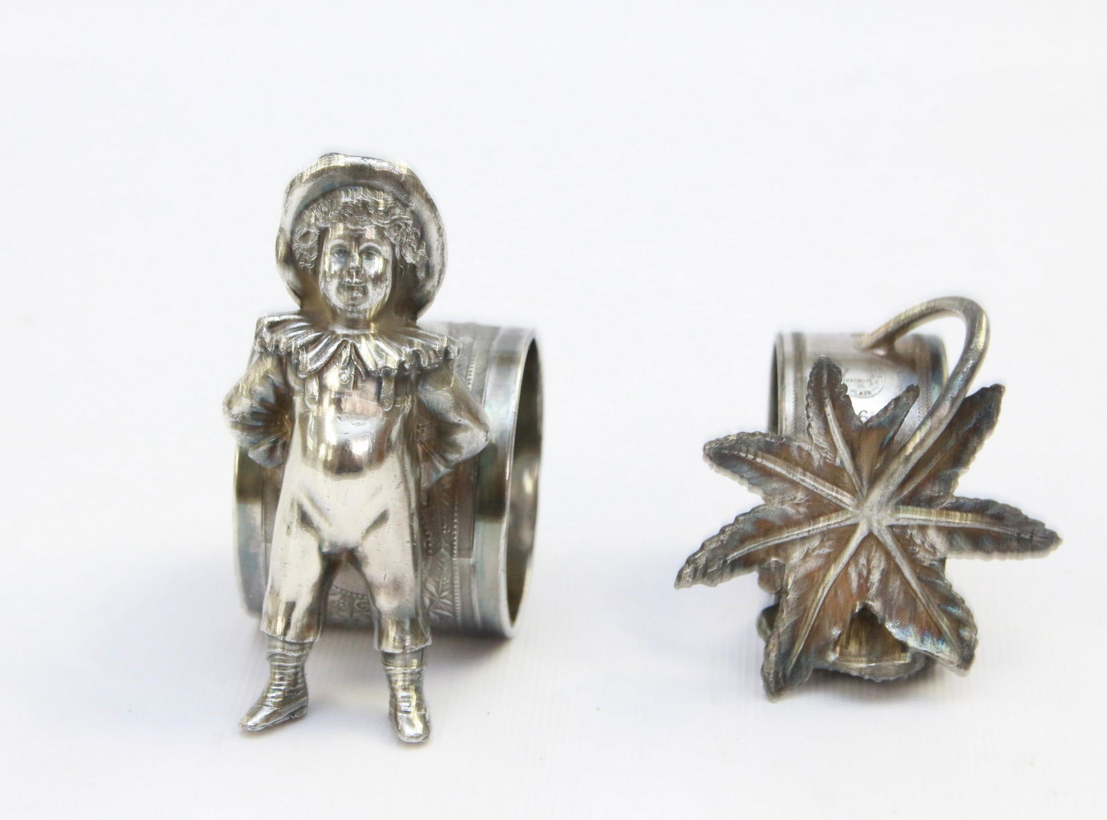 PAIR OF FIGURAL NAPKIN RINGS: INCLUDES: CHILD IN OVERALLS MONOGRAMMED "WATSON" AND LEAF/FLOWER MRKD. QUADRUPLE PLATE Size: 2" TO 3 1/4" H