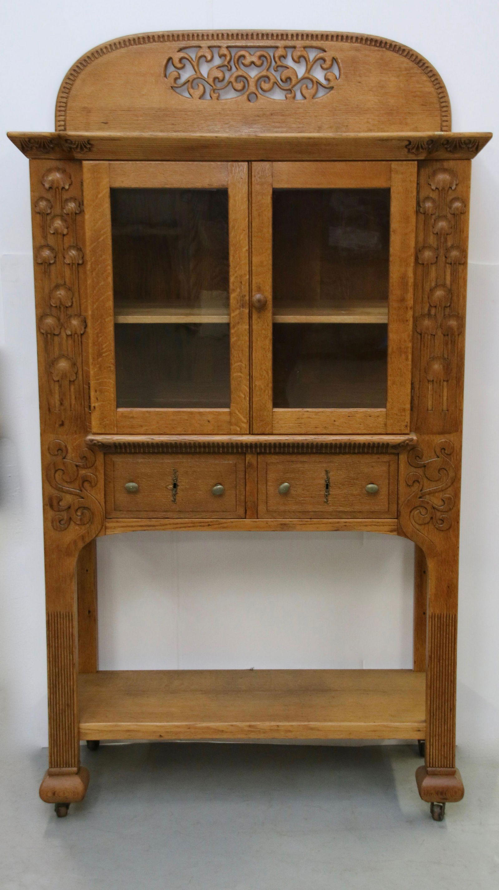 OAK ART NOUVEAU STYLE CABINET: TWO GLASS DOORS OVER TWO DRAWERS OVER BOTTOM OPEN SHELF. APPLIED TREE DECORATION. HEART CUT-OUT AT TOP. BRASS HARDWARE. LIGHTED INTERIOR. Size: 69" H X 39" X 18" Important Shipping Information: We d