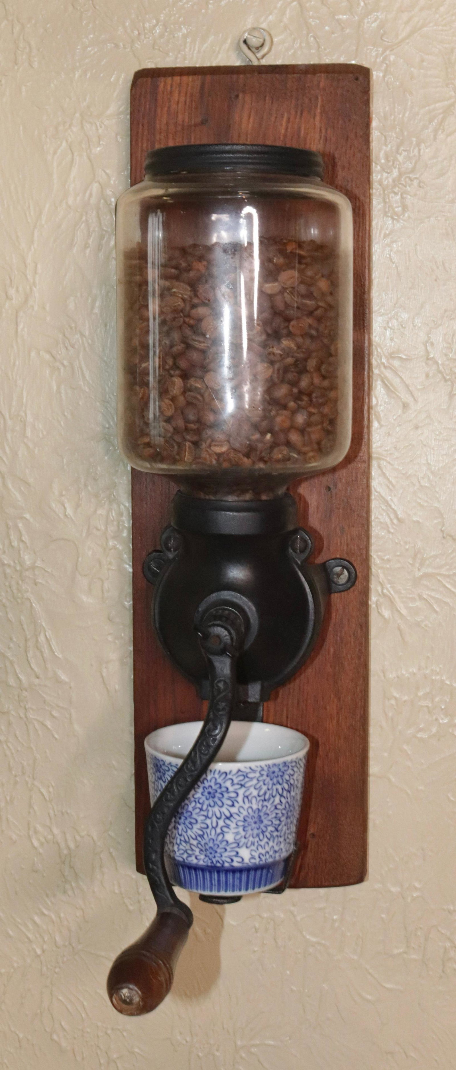 ANTIQUE COFFEE GRINDER: CAST IRON AND WOOD - WALL MOUNTED WITH BLUE AND WHITE CUP (NOT ORIGINAL) SIZE: 17 3/4" H