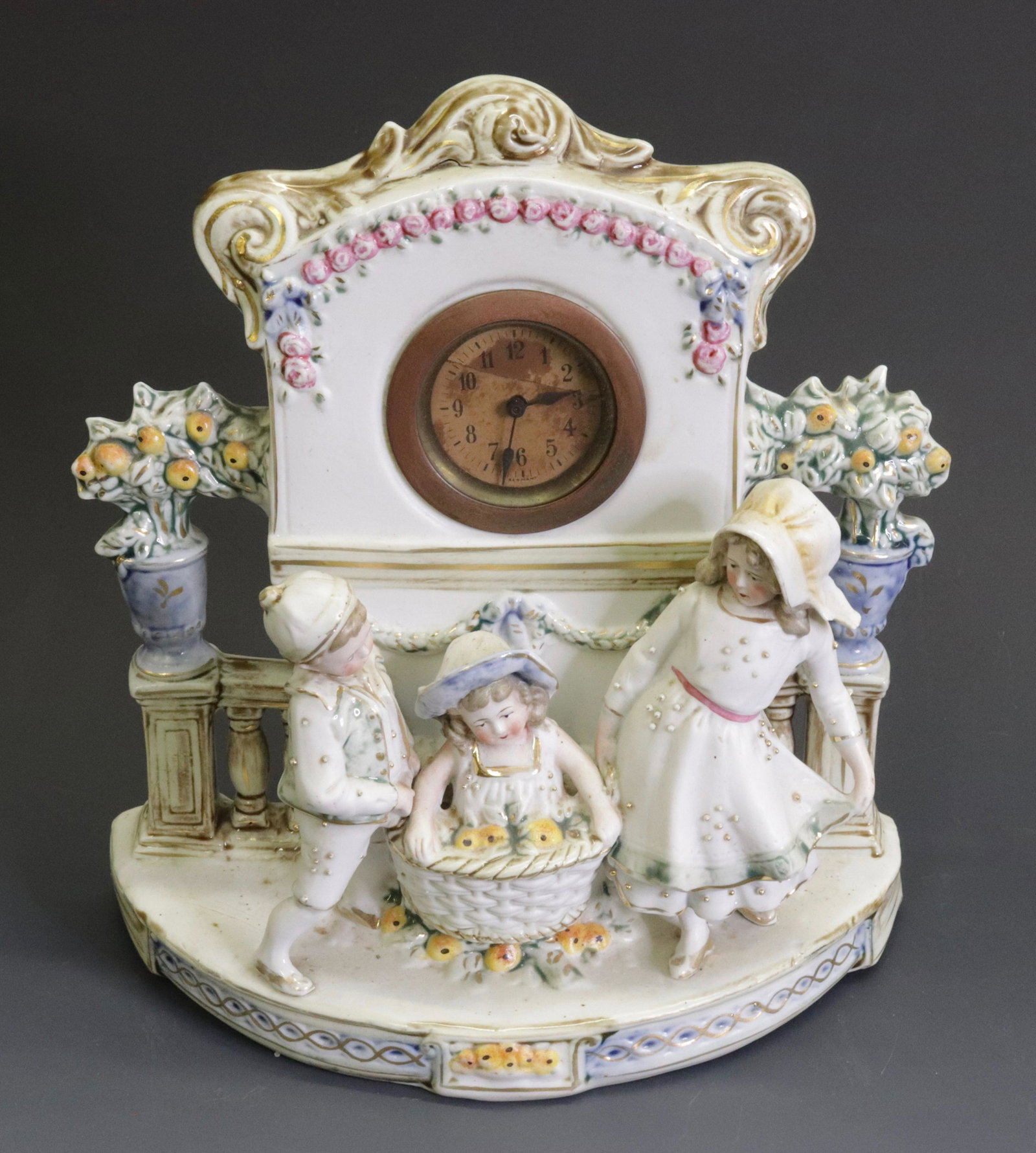 HAND PAINTED GERMAN PORCELAIN SHELF CLOCK: DEPICTS CHILDREN WITH FRUIT BASKET. STAMPED GERMANY ON BOTTOM. 10" X 9.5"
