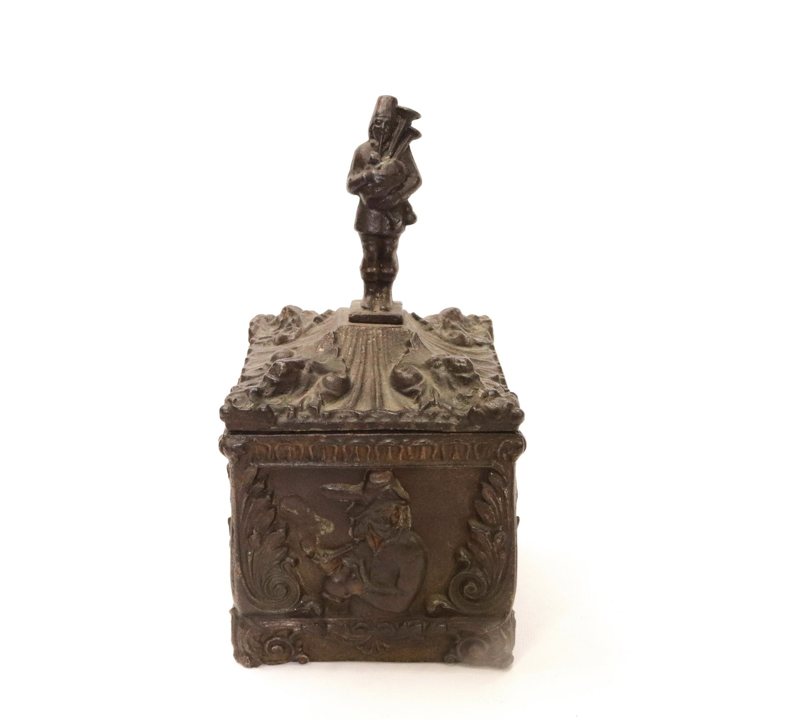 RARE 19TH CENTURY CAST IRON TOBACCO BOX: FOUR SIDED BOX WITH SCENES DEPICTING FIGURES DANCING AND SMOKING - BAGPIPE PLAYER TOP FINIAL ON LID - TRACES OF ORIGINAL PAINT 11" H 5" X 5"