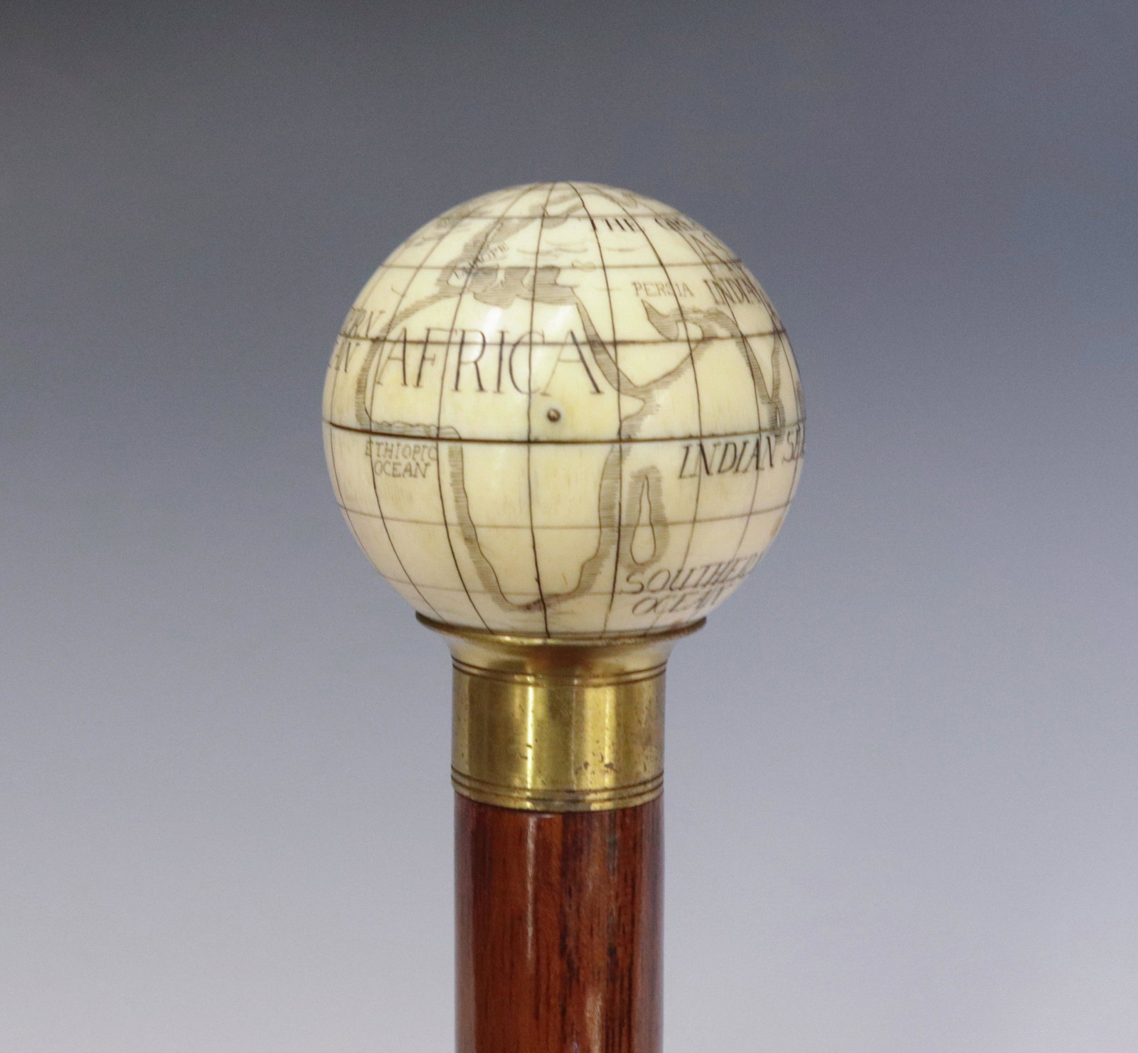 CARVED BONE GLOBE COMPASS CANE: BONE KNOB CARVED AS A GLOBE WITH HINGED TOP THAT LIFTS TO REVEAL COMPASS UNDER GLASS WINDOW - BRASS COLLAR AND HARDWOOD SHAFT 35 1/4" L