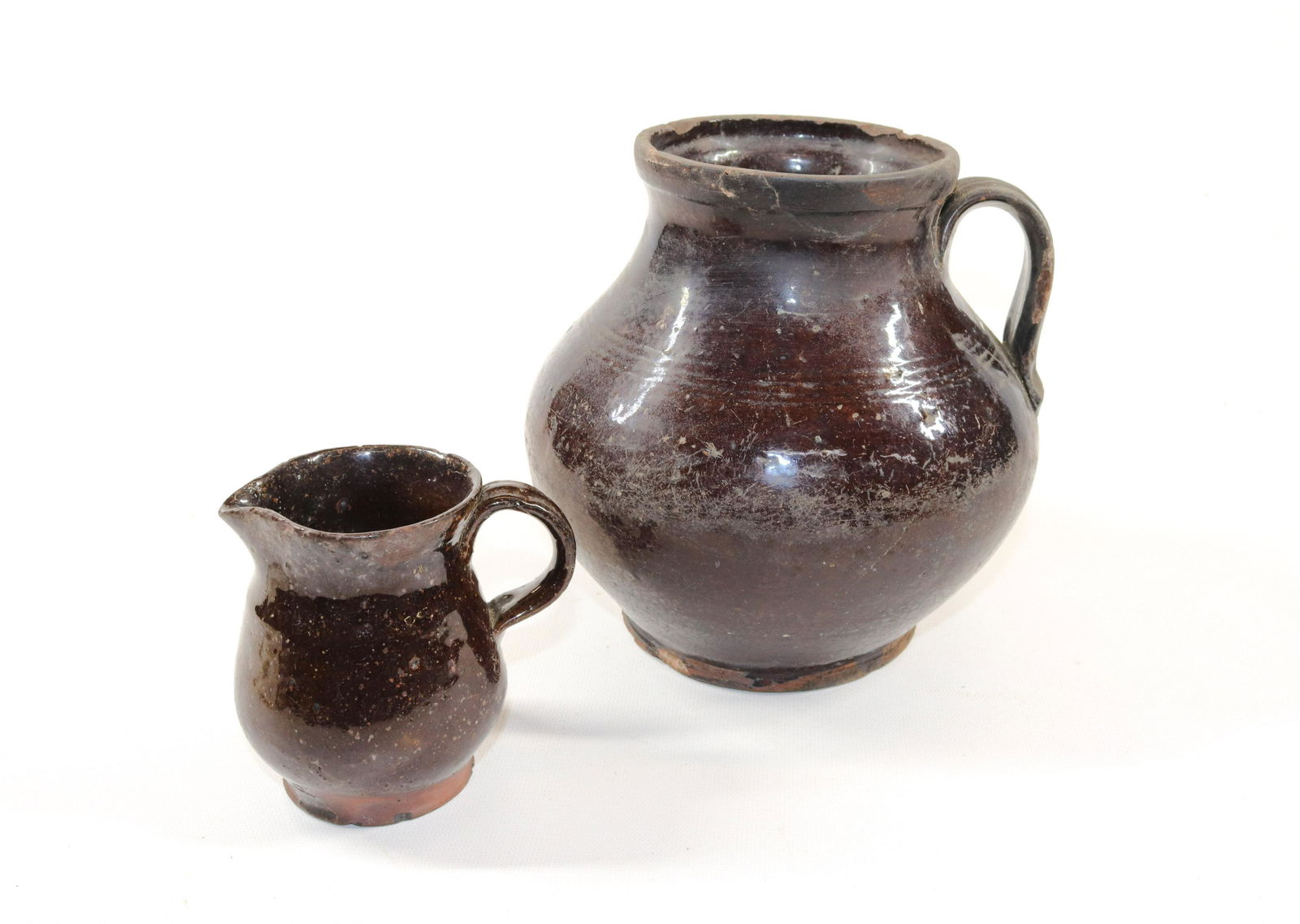 PAIR OF REDWARE POTS: INCLUDING: OVOID POT WITH STRAP HANDLE AND CREAMER. BOTH IN DARK GLAZE Size: 4" TO 7 1/2" H