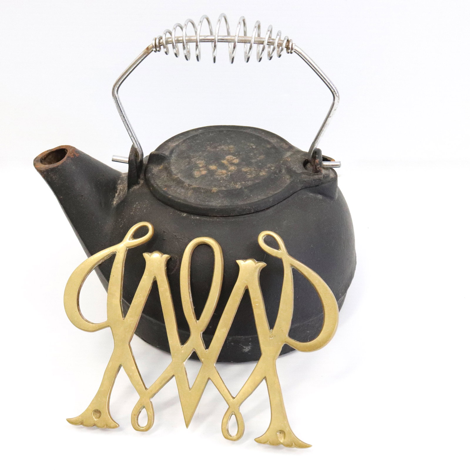 Cast iron teapot and trivet: Description: Cast iron pot with metal handle - brass trivet marked "1950 williamsburg" Condtion: Lid of pot broken at attachment point Size: POT 10 1/2" WIDE Consignor: JS Terms: This is an On-Site