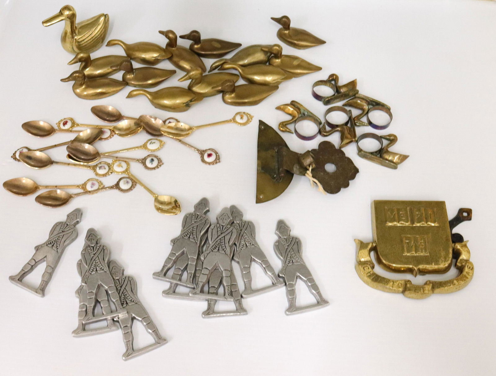 Brass and metal home furnishing lot: Description: Including - (14) brass ducks, (5) napkin rings, gold toned spoons with floral motif, cast metal soldiers, and more Condtion: Wear consistent with age and use Size: DUCKS 3 1/2" L - SPOONS