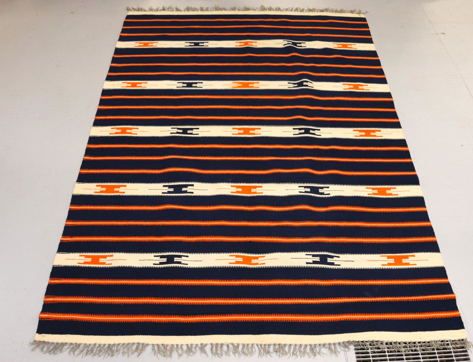 VINTAGE HANDWOVEN RUG: NAVY/ORANGE/CREAM WITH FRINGE Dimensions 77" X 52" PLEASE READ BEFORE BIDDING – PICKUP FOR THIS AUCTION WILL NOT BE UNTIL THE WEEK OF OCTOBER 25TH. PICK-UP WILL BE FROM 9:00AM TILL 4:00PM –