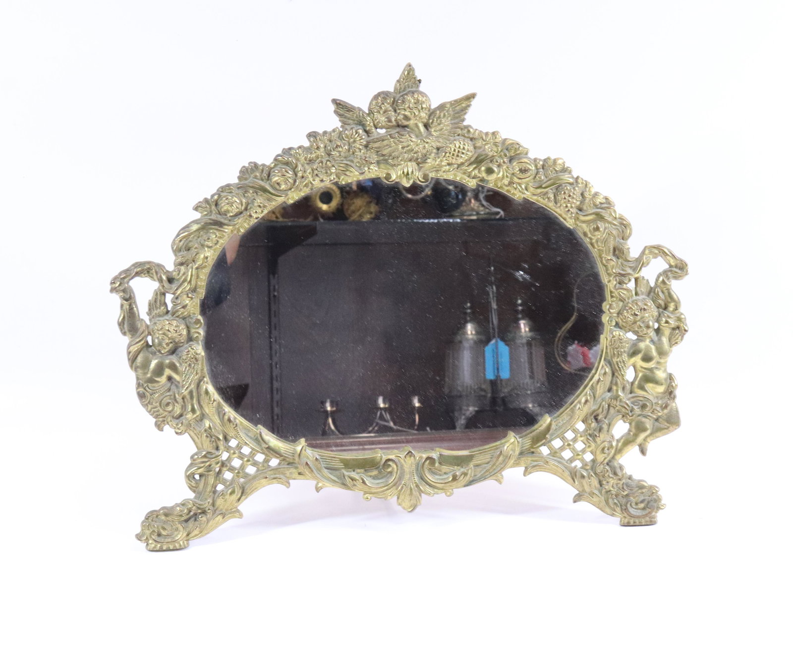 CAST IRON TABLE MIRROR: ORNATE BRASS PLATED FRAME WITH CUPIDS AND PUTI, ORIGINAL BACK AND STAND SIZE: 13" X 16" PLEASE READ BEFORE BIDDING – PICKUP FOR THIS AUCTION WILL NOT BE UNTIL THE WEEK OF OCTOBER 25TH. PICK-UP WILL 