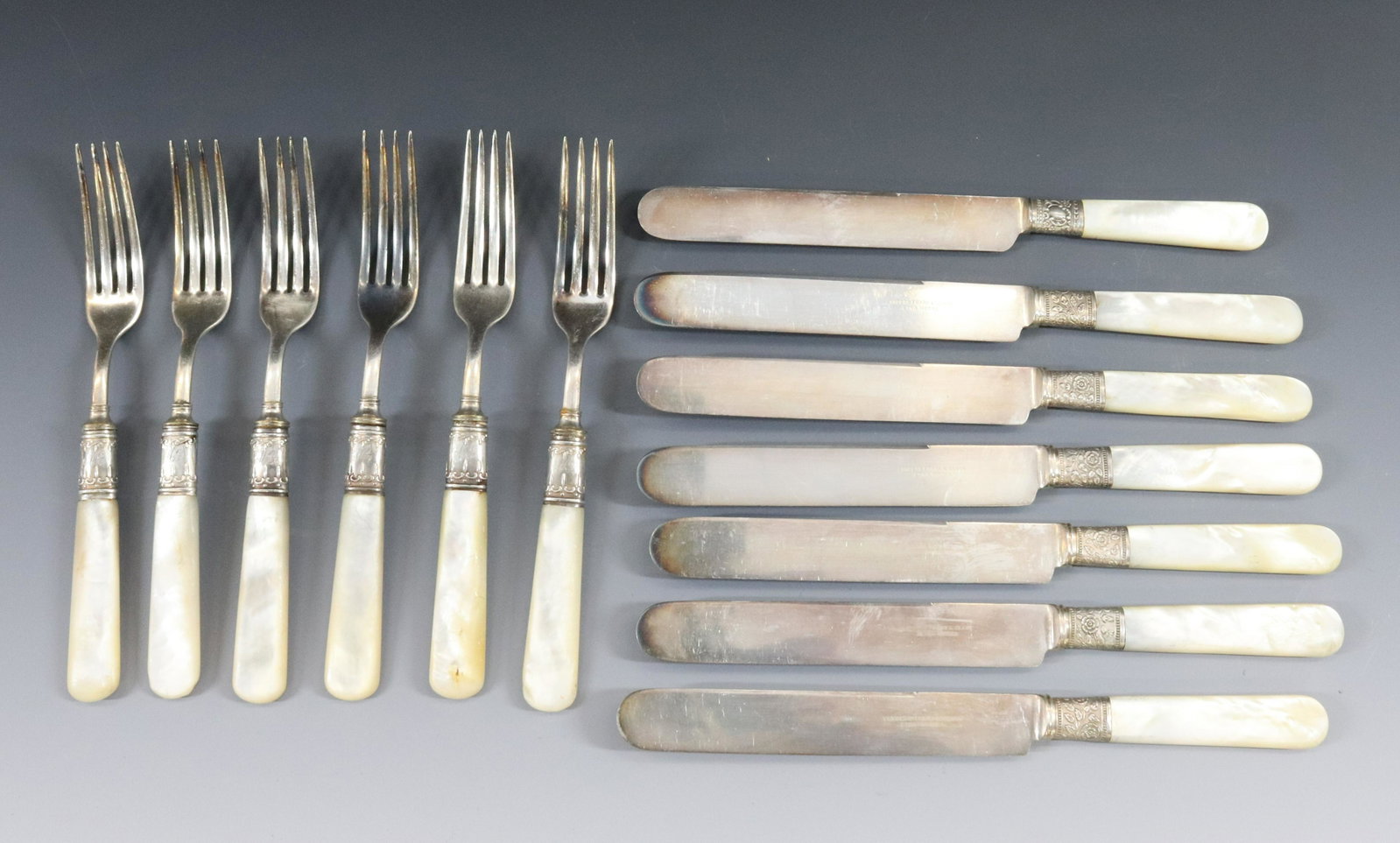 SILVER PLATE AND MOTHER OF PEARL FLATWARE: (13) INCLUDES SIX FORKS SEVEN KNIVES WITH STERLING SILVER BANDS NOTE TWO DIFFERENT PATTERNS ON BANDS DIMENSIONS: KNIFE 9 1/4" FORK 7 5/8" TERMS: Hartzell's Auction Gallery will handle most of the ship