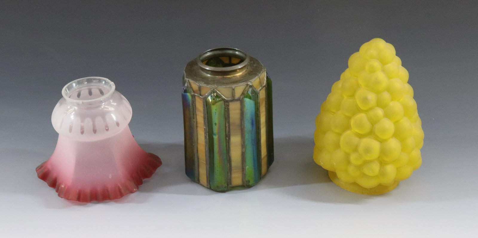 GLASS LAMP SHADES GROUP: (3) LEADED GLASS WITH IRIDESCENT GREEN PRISMS, GRAPE SHADE YELLOW AND RUFFLED CRANBERRY RIM SHADE DIMENSIONS: LEADED 5 1/2"H X 2 1/4" FITTER, 6 1/2" X 3 1/4" FITTER, 4 1/2" X 2 1/4"FITTER TERMS: Hartz