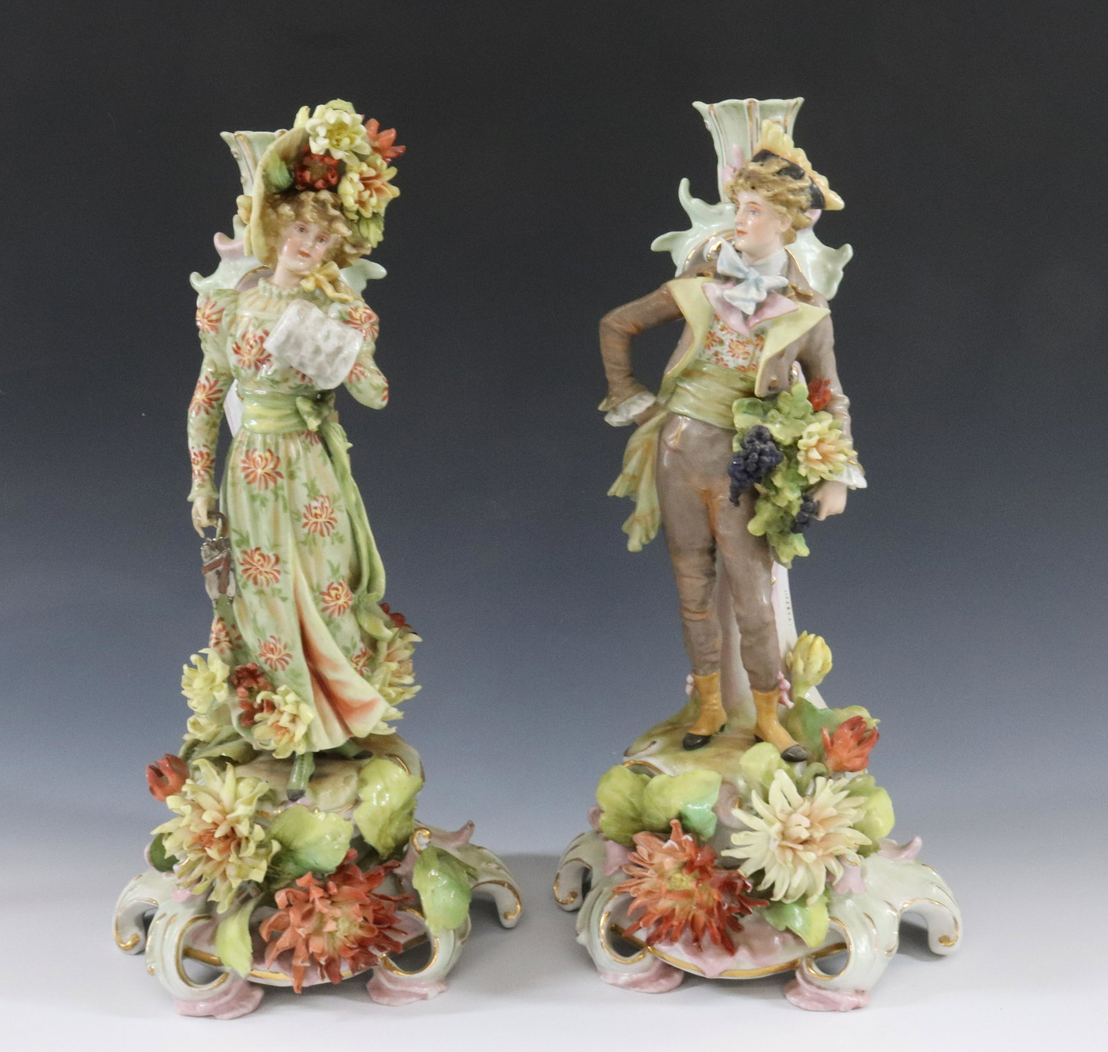 GERMAN ORNATE PORCELAIN CANDLESTICKS: (2) CANDLESTICKS OR CANDELABRA BASES YOUNG LADY WITH MUFF AND LARGE HAT NICE DETAILS FACES AND CLOTHING UNMARKED DIMENSIONS: 13 1/2" X 6 1/2" TERMS: Hartzell's Auction Gallery will handle most of the 