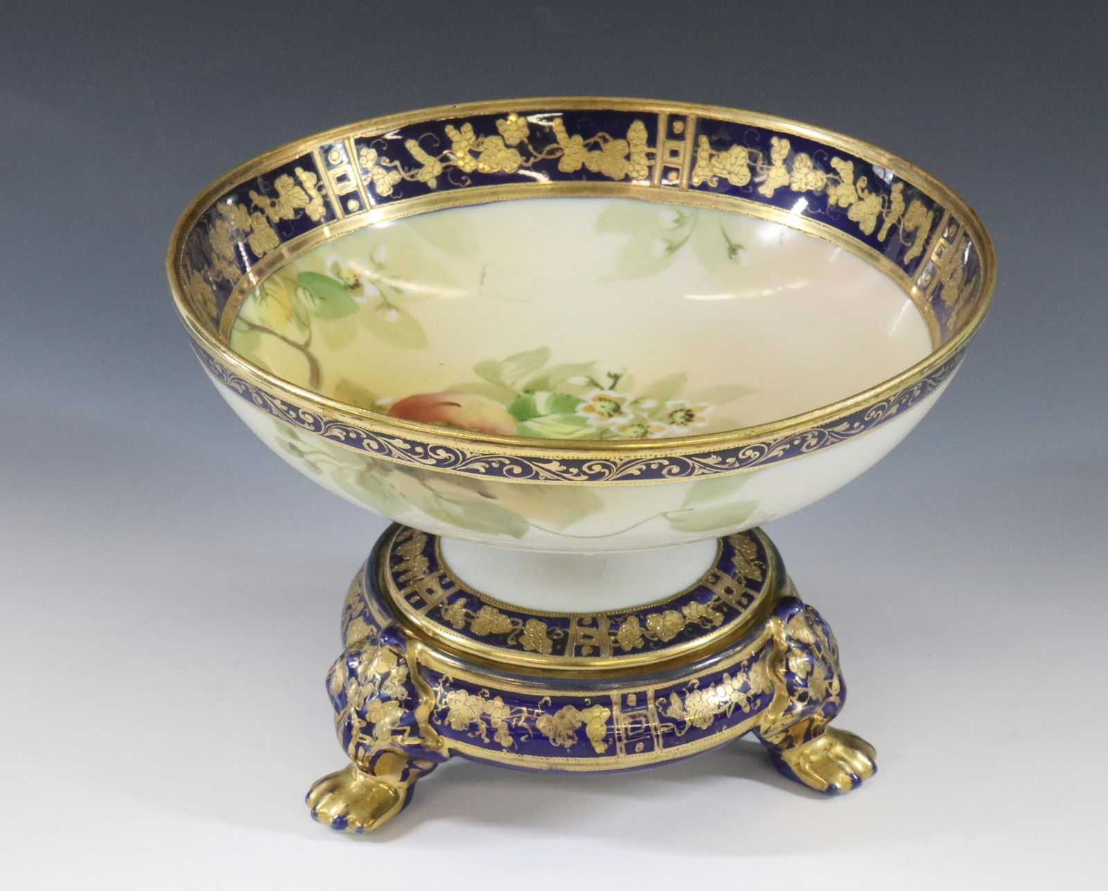 NIPPON COMPOTE AND STAND: HAND PAINTED FRUIT WITH COBALT AND GOLD BORDER DIMENSIONS: 7"H X 10"DIA TERMS: Hartzell's Auction Gallery will handle most of the shipping in-house. WE do reserve the right to not ship some large item