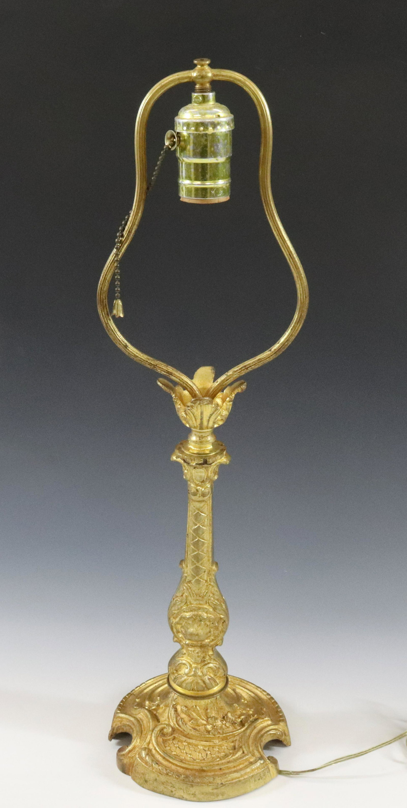FRENCH ROCOCO TABLE LAMP: CAST BRASS WITH GOLD WASH SINGLE LIGHT AND HARP 1930S DIMENSIONS: 19 1/2"H X 5"DIA TERMS: Hartzell's Auction Gallery will handle most of the shipping in-house. WE do reserve the right to not ship some