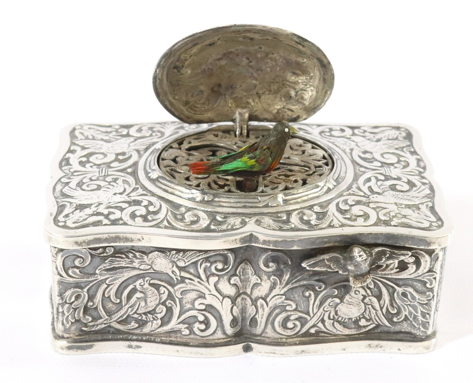 SILVER ORNATE MUSIC AUTOMATON BOX: GERMAN HAND CHASED SILVER BOX WITH BIRDS FLOWERS AND VINE SINGING BIRD AUTOMATON KEY WIND WITH REPLACED KEY. DIMENSIONS: 1 7/8" X 4" X 2 1/2" TERMS: Hartzell's Auction Gallery will handle most of the 