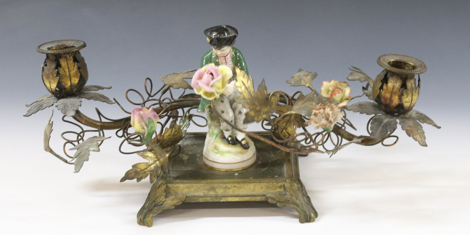 FRENCH LOW CANDELABRA: BRASS CAST BASE WITH BRASS LEAVES PORCELAIN FLOWERS AND FIGURINE OF GENTLEMAN DIMENSIONS: 5 1/2"h x 14" x 6" TERMS: Hartzell's Auction Gallery will handle most of the shipping in-house. WE do reserve 