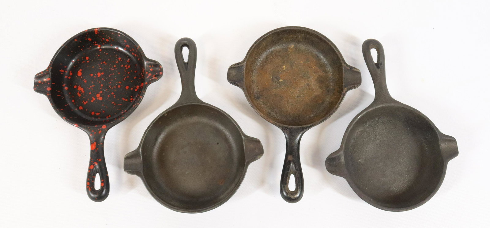 LOT OF WAGNER WARE CAST IRON ASHTRAYS: THREE MRKD. WAGNER WARE 1050B AND 1050E. PLUS, BLACK/RED PORCELAIN SPECKLED EXAMPLE. MEASURE 6 1/4" TOTAL LENGTH.