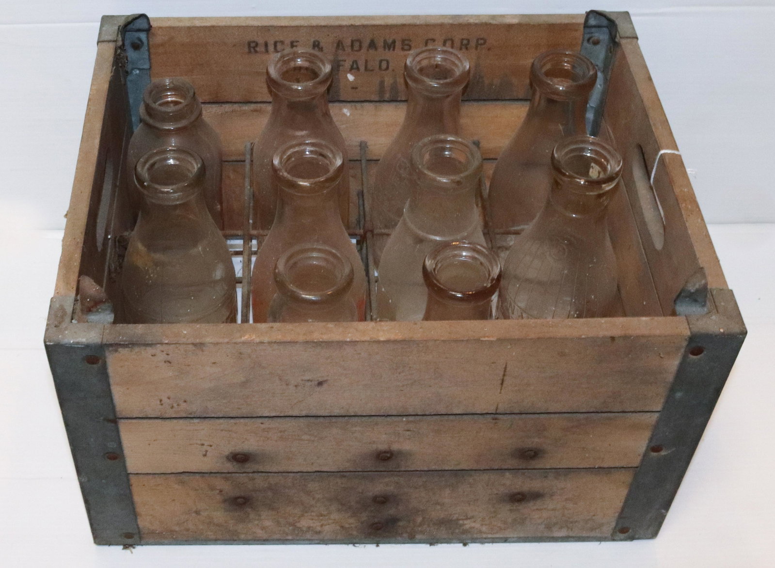 WOODEN MILK CRATE AND (10) MILK BOTTLES: CRATE IS MRKD. RICE&ADAMS CORP., BUFFALO, NY. BOTTLES INCLUDE: PENN-DELL (STROUDSBURG), SHEFFIELD, SNYDERS (STROUDSBURG), HAMILTON DAIRY (STROUDSBURG) AND MORE. CRATE MEASURES 10 1/2" X 18 1/2" X 14 1