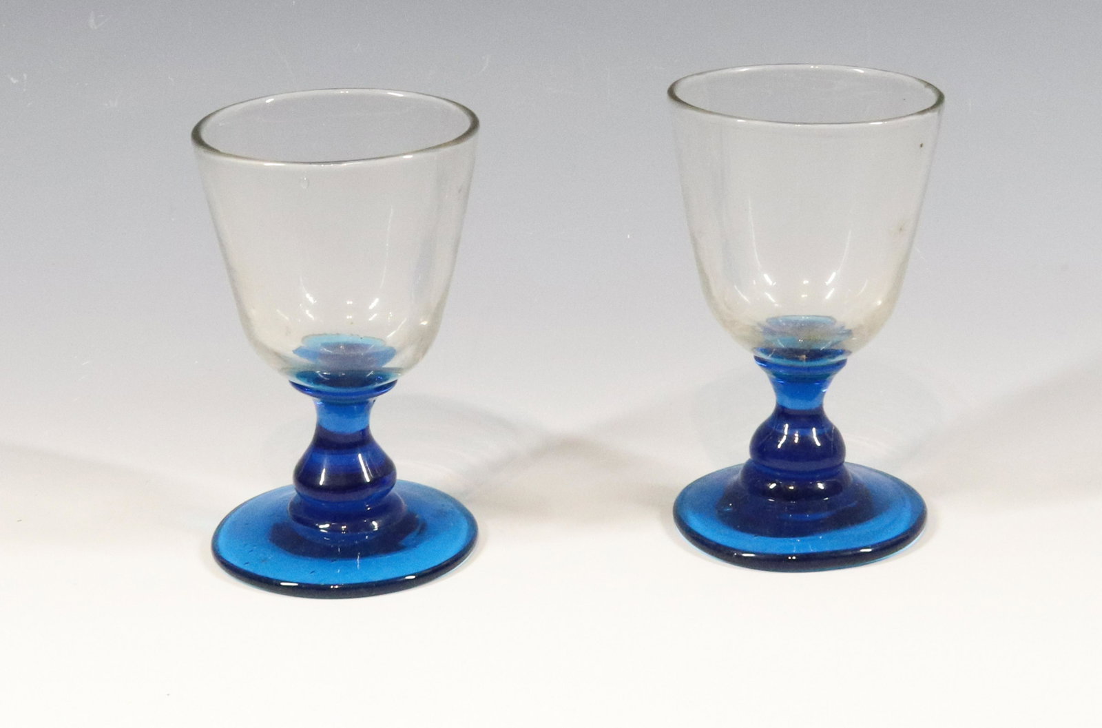 (2) PITTSBURGH WINE GLASSES: FREE BLOWN WITH DEEP ELECTRIC BLUE BASE AND STEM POLISHED PONTILS NON-FLINT 1860/70 ERA 4 1/2" X 2 3/4' Please Read Carefully before Bidding. Hartzell’s Auction Gallery Inc. will Conduct an ON-S