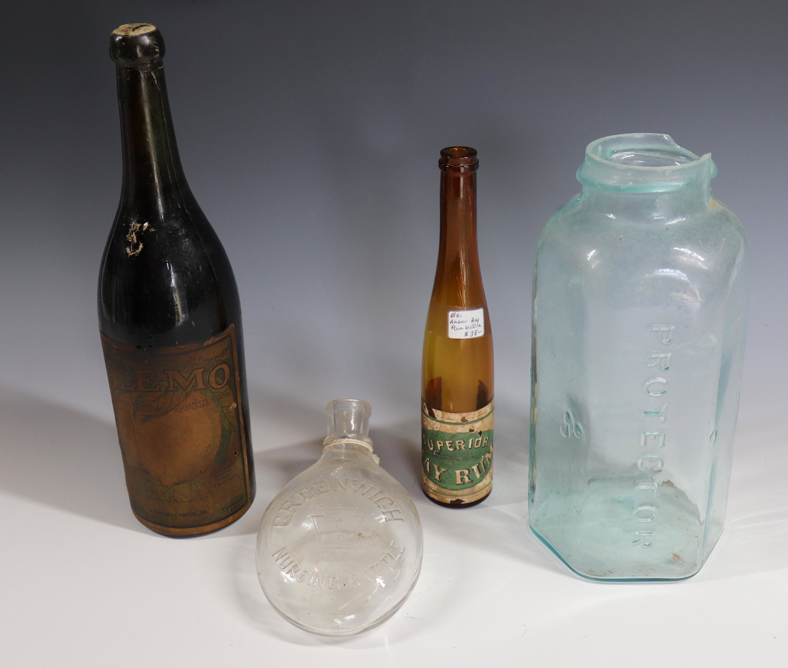 (4) BOTTLES: BAY RUM WITH LABEL, FULL WINE BOTTLE OLEMO, GREENWICH NURSING BOTTLE AND PROTECTOR FRUIT JAR 6" TO 12" Terms: Please Read Carefully before Bidding. Hartzell’s Auction Gallery Inc. will Conduct an ON
