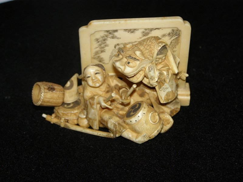 CARVED IVORY NETSUKE - WOMAN PLAYING DRUM AS LADY: CARVED IVORY NETSUKE - WOMAN PLAYING DRUM AS LADY DANCES WITH DRAGON HEAD DRESS WITH CARVED IVORY BIRD DECORATED SCREEN. 4" x 2" x 2 1/2"