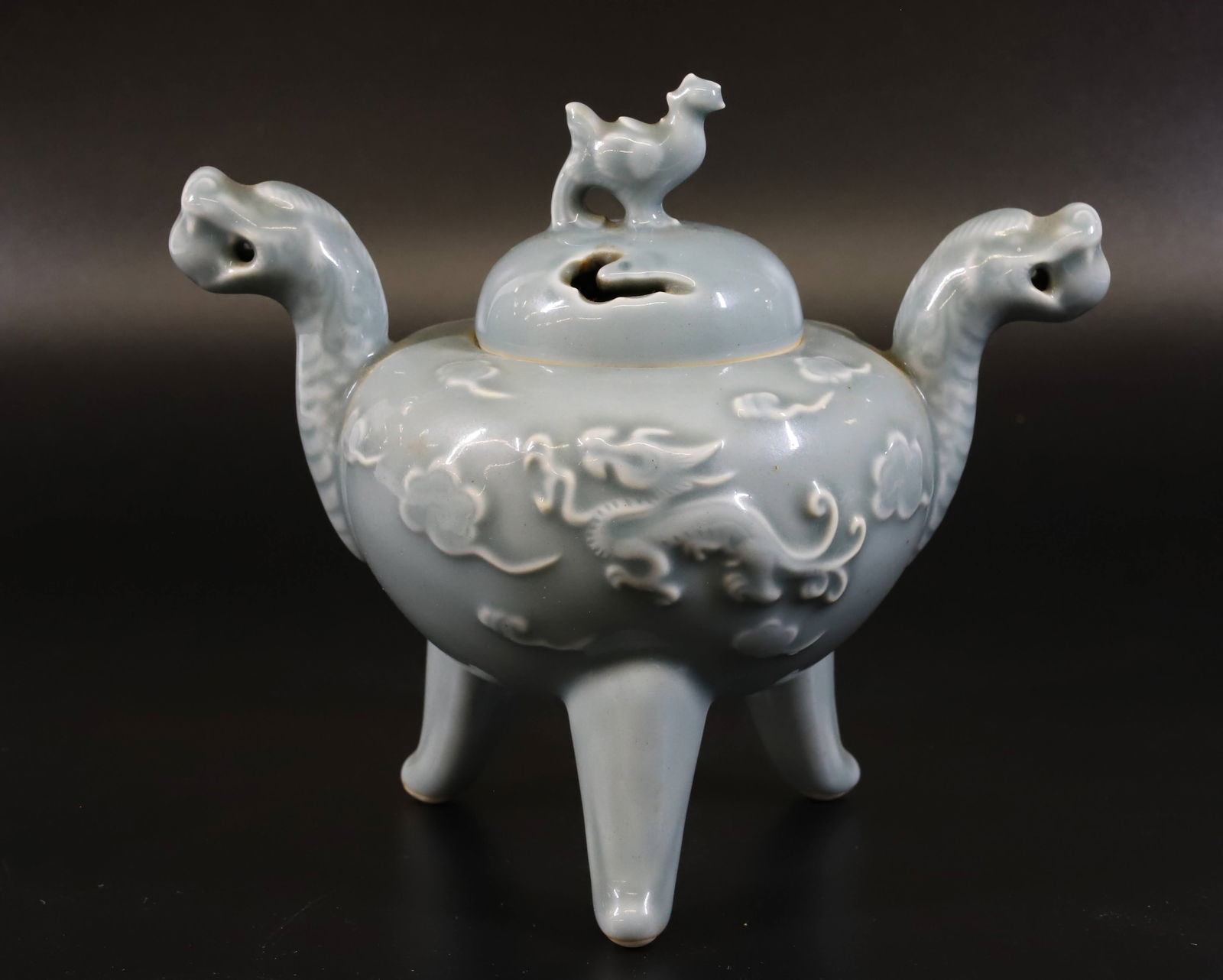 NABESHIMA INCENSE BURNER: CELADON GLAZE WITH BLUE MARKINGS ON BOTTOM. DRAGON HEADS AND BIRD FINIAL ON LID. EMBOSSED DRAGON ON EITHER SIDE. 6 3/4" X 7 1/2". PLEASE READ CAREFULLY - Terms for Purchasing and Shipping of Auction I