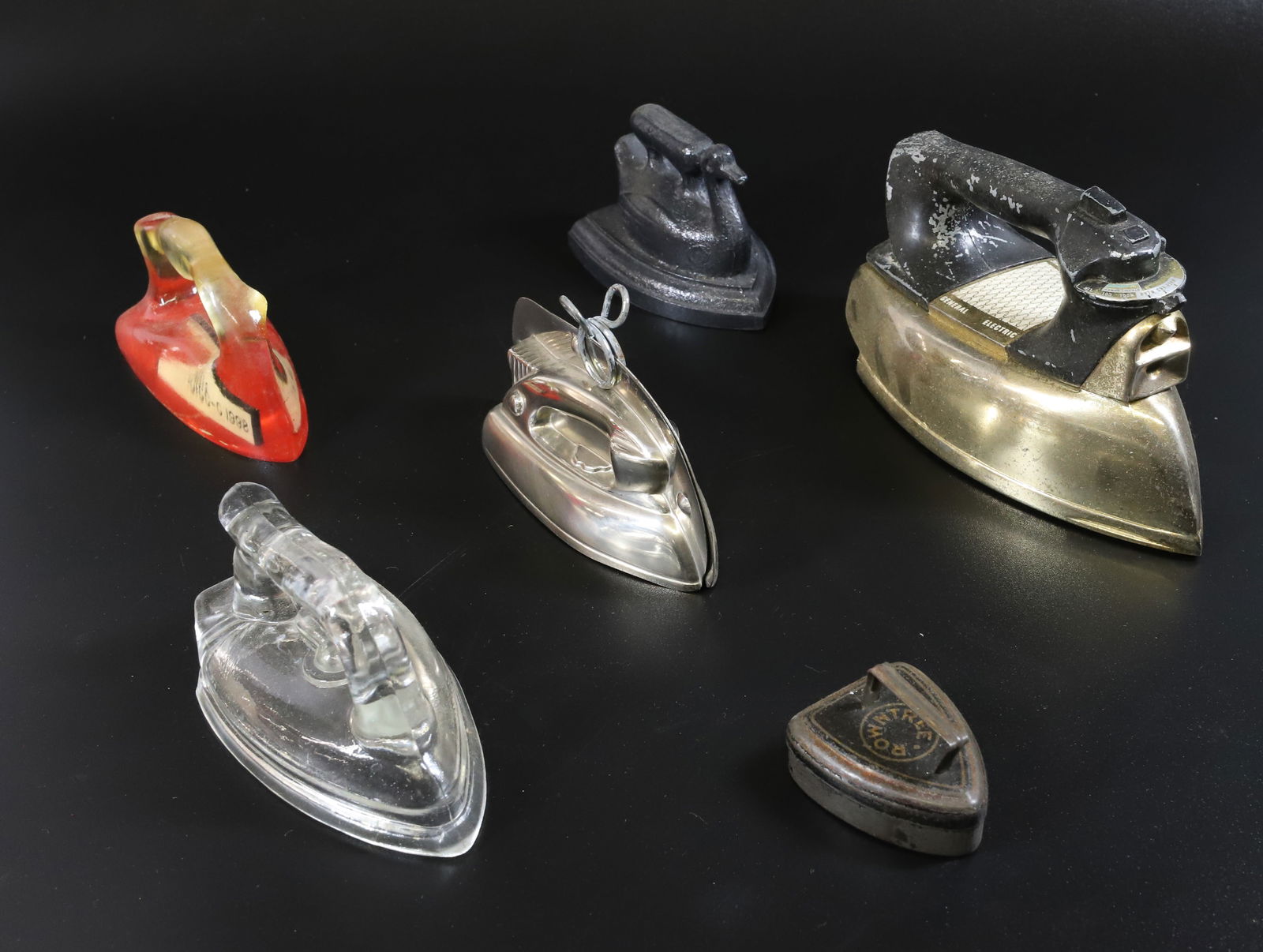LOT OF TOY IRONS: (6) IRONS INCLUDING - GLASS IRON COVER, PLASTIC SWAN, TIN SAD IRON, PLASTIC RED AND CLEAR IRON, AND GENERAL ELECTRIC PLEASE READ CAREFULLY - Terms for Purchasing and Shipping of Auction Items. Please