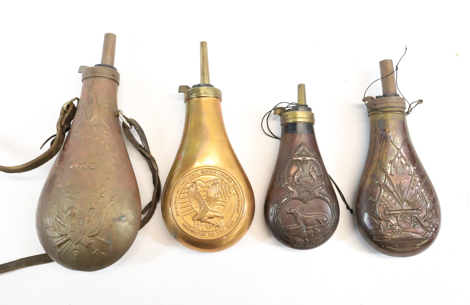 LOT OF POWDER FLASKS: (4) COPPER AND BRASS POWDER FLASKS - IMPRESSED EAGLE AND US SHIELD, CANNON, DOGS AND BIRDS, AND OTHER - LARGEST 9" UPDATED 2024 TERMS FOR PURCHASING AND SHIPPING OF AUCTION ITEMS. PLEASE READ CAREFULL