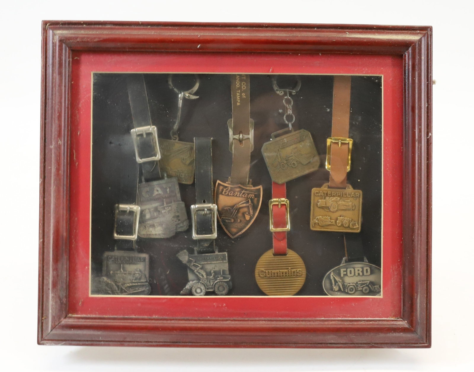 LOT OF MACHINERY WATCH FOBS/KEY CHAINS: INCLUDING: CATERPILLAR, FORD, BANTAM, CUMMINS, CAT AND MORE. IN SHADOW BOX FRAME. 9 1/2" X 11 1/2". PLEASE READ CAREFULLY - Terms for Purchasing and Shipping of Auction Items. Please read carefully be