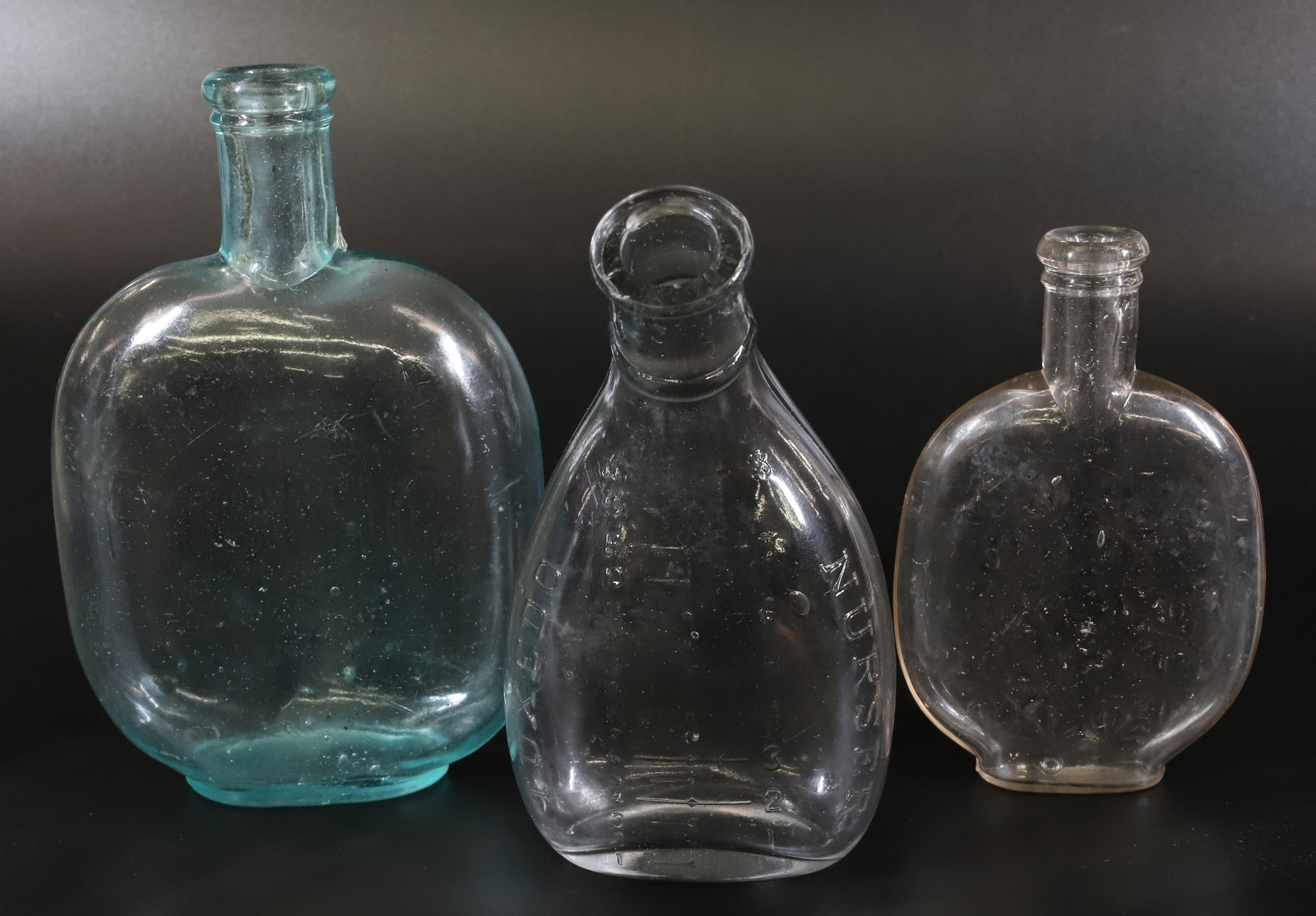 (2) FLASKS AND NURSING BOTTLE: AQUA "PICNIC FLASK", EMBOSSED CLEAR FLASK AND CLEAR TUXEDO NURSER. 5 1/4" TO 6 3/4" HEIGHTS. PLEASE READ CAREFULLY - Terms for Purchasing and Shipping of Auction Items. Please read carefully before bi