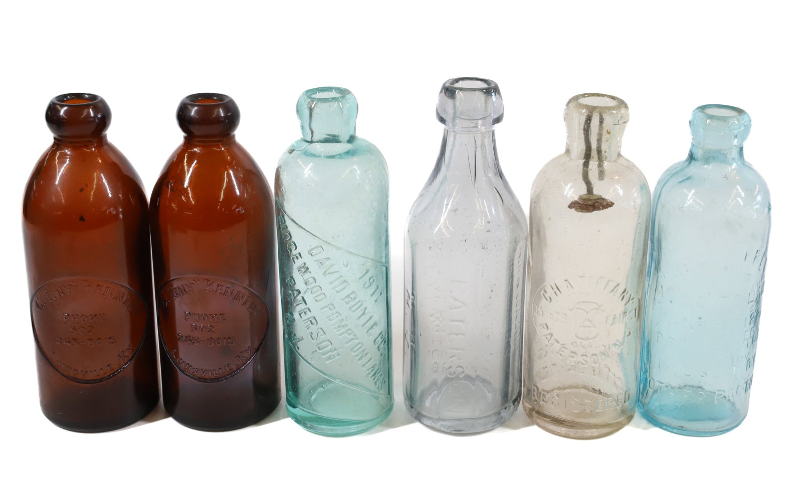 LOT OF NJ AND KY BOTTLES: (4) PATERSON INCLUDING: CHA. TIFFANY, TIFFANY & ALLEN MINERAL WATER, DAVID BOYLE 1911, CHA. TIFFANY (CLEAR). (2) C. "TINY" KENNEDY AMBER "LOUISVILLE, KENTUCKY" BOTTLES. 6 1/2" TO 7" HEIGHTS. PLEASE RE